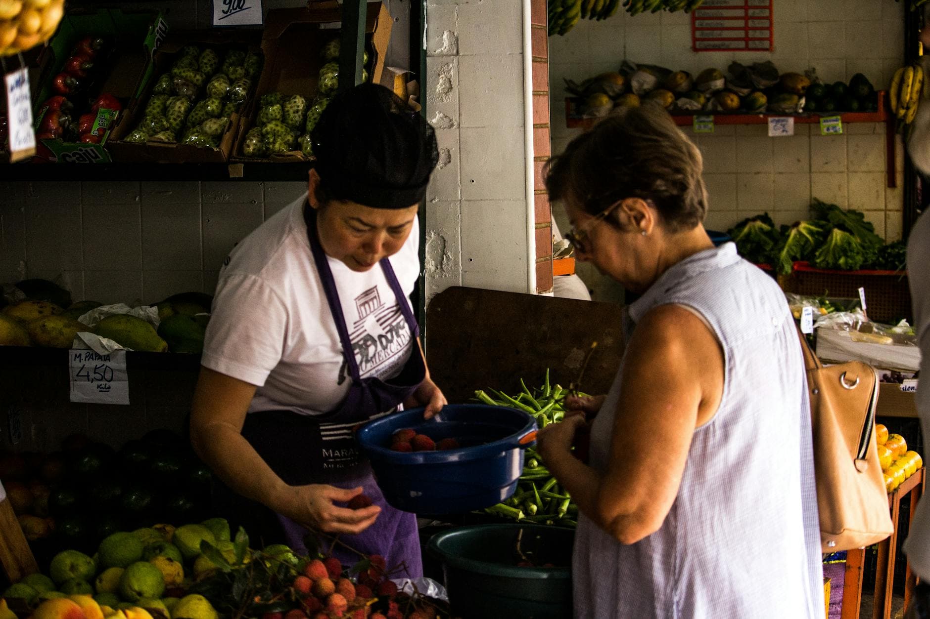 Two women interacting over fresh produce in an outdoor market setting. - healthy snacks to buy