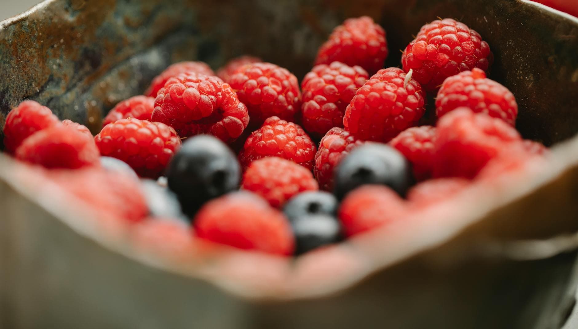 Close-up of fresh raspberries and blueberries in a metal bowl. Vibrant and healthy. - protein foods for weight loss
