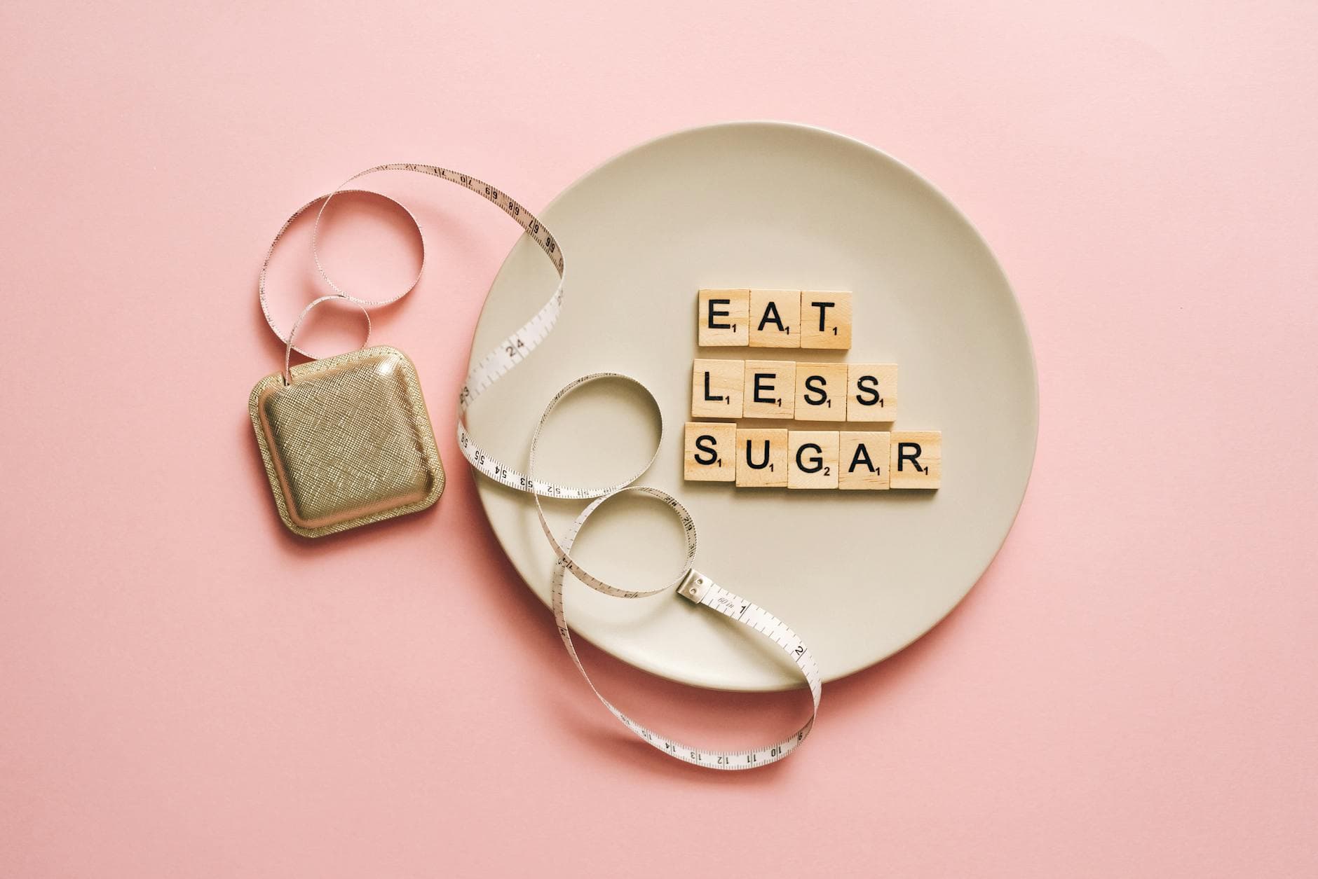Flat lay of Scrabble tiles saying 'Eat Less Sugar' on a plate with a tape measure on a pink background. - extreme weight loss