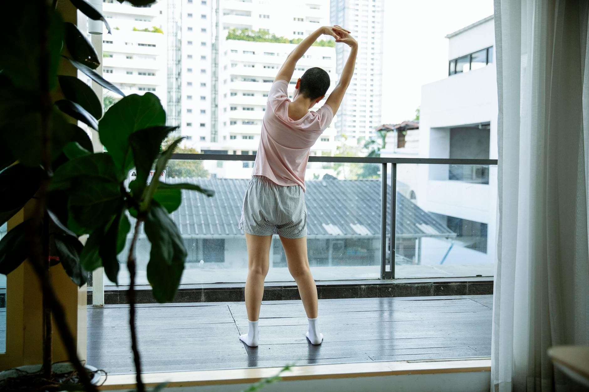 Back view of anonymous female suffering from cancer stretching on glass balcony in hospital - lower back stretches