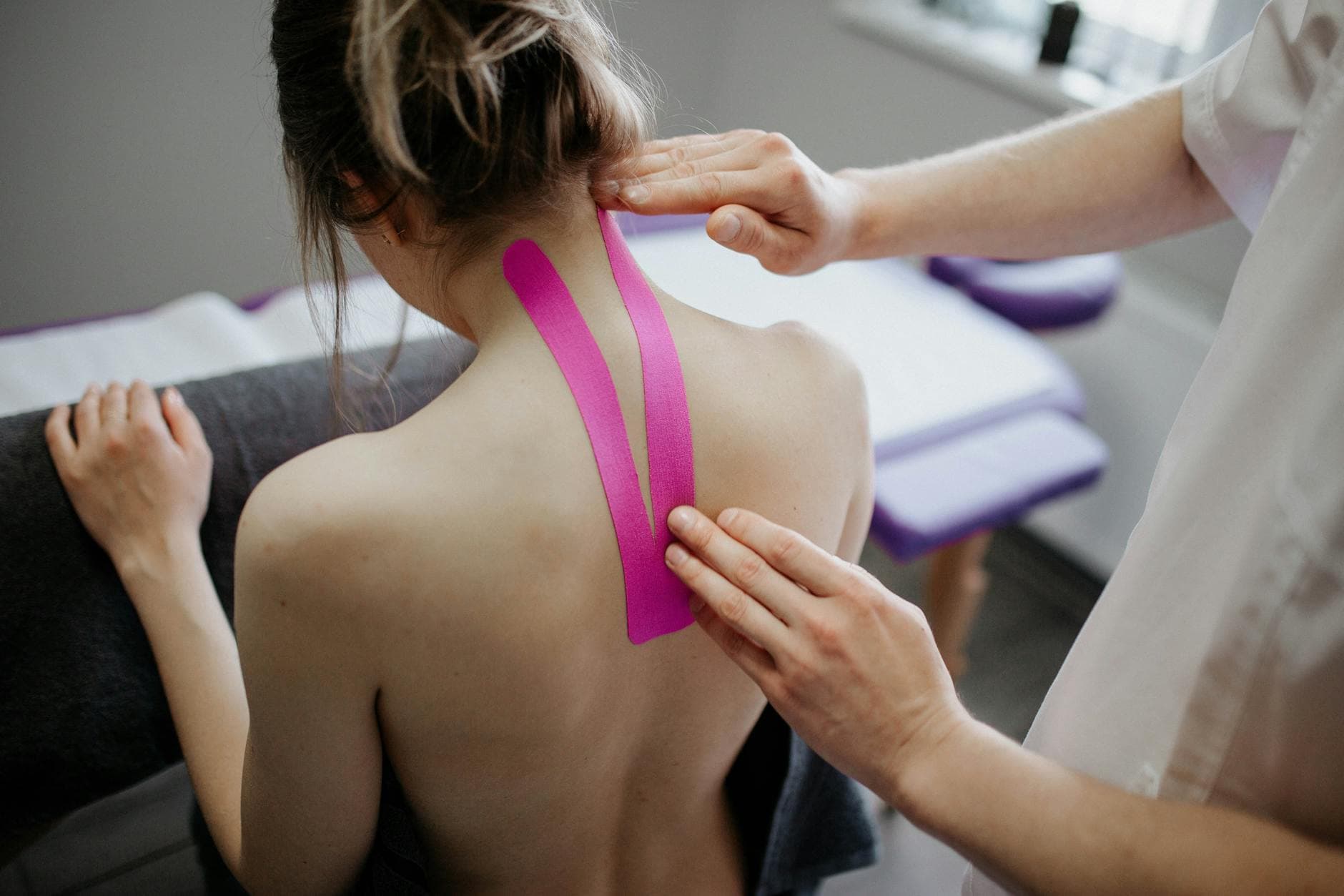 A healthcare professional applies kinesiology tape on a woman's neck for therapeutic treatment. - pregnant back pain