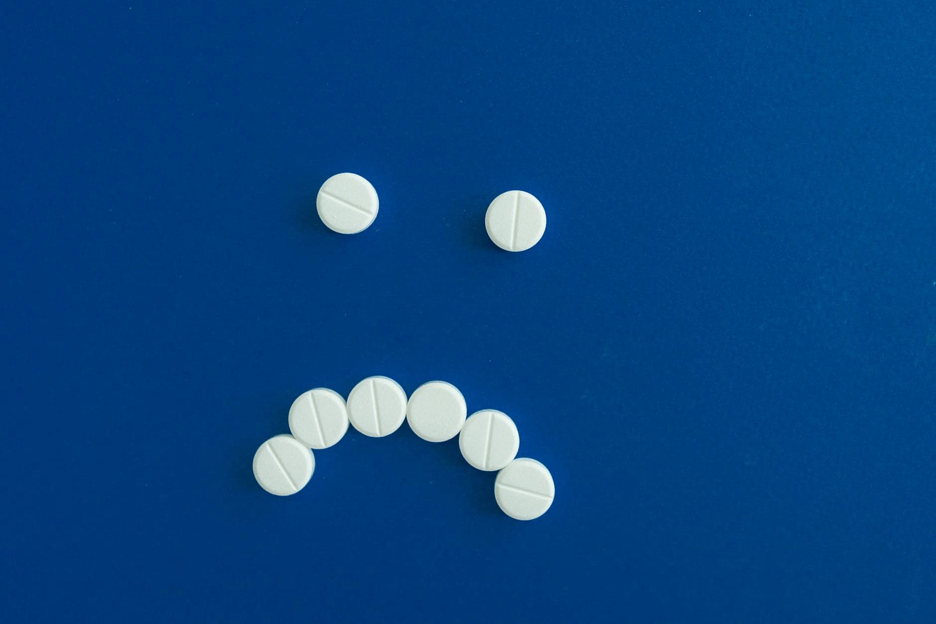 White pills arranged in a sad face shape on a solid blue background. - spring sad science