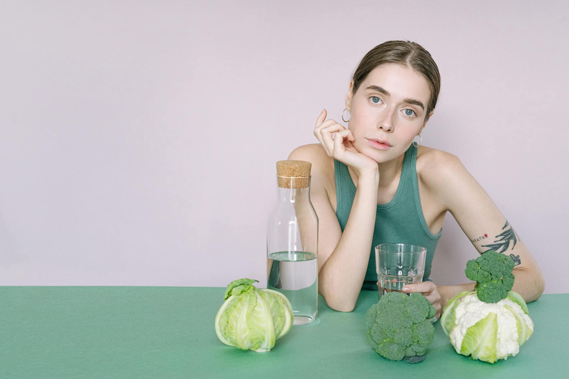A young woman in a green top sitting with vegetables and a glass of water. - body detox diet