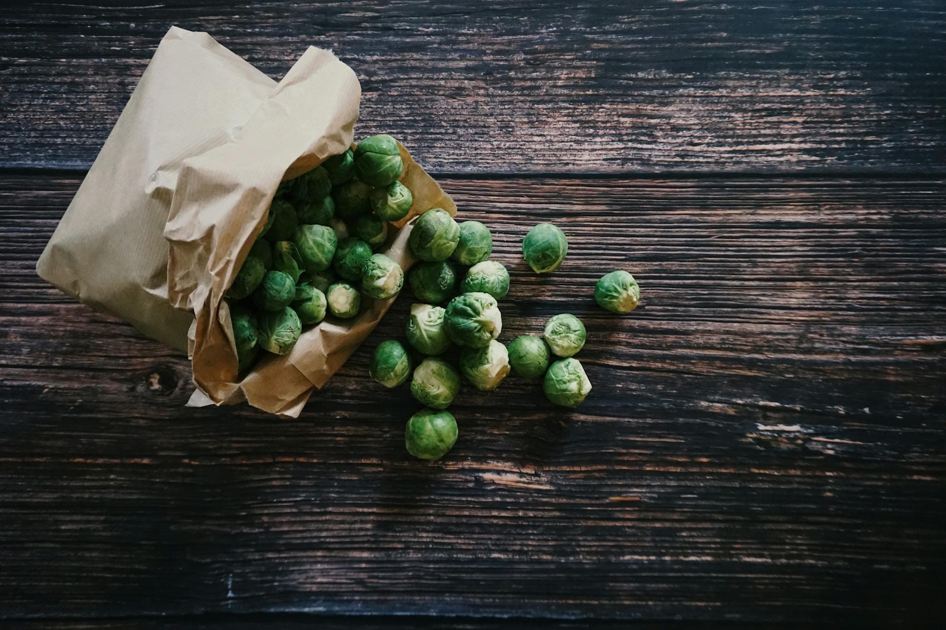 Fresh Brussels sprouts poured from a paper bag onto a rustic wooden table. - healthy casserole recipes