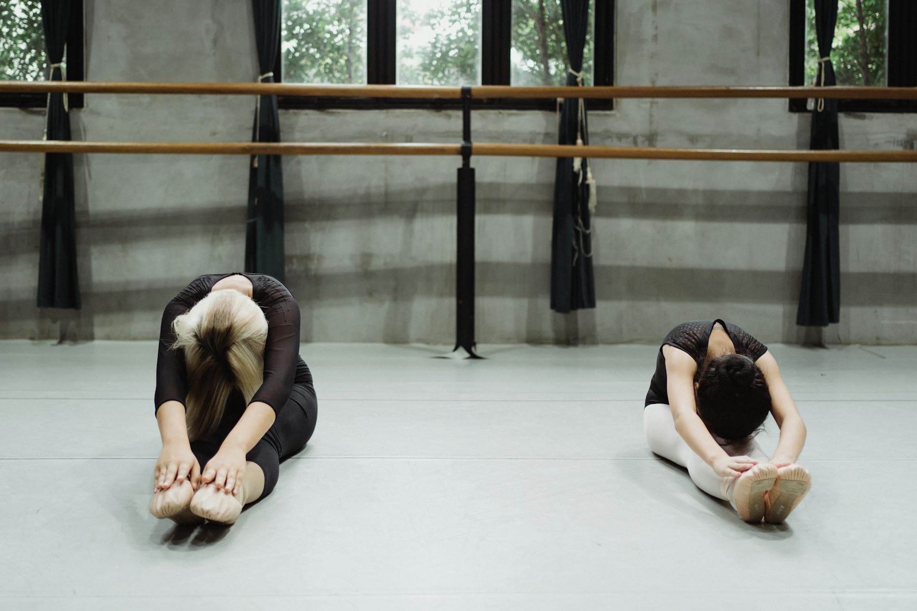 Full body of anonymous young and teenage female dancers in activewear and pointes doing Seated Forward Bend exercise during ballet training in studio - lower body flexibility