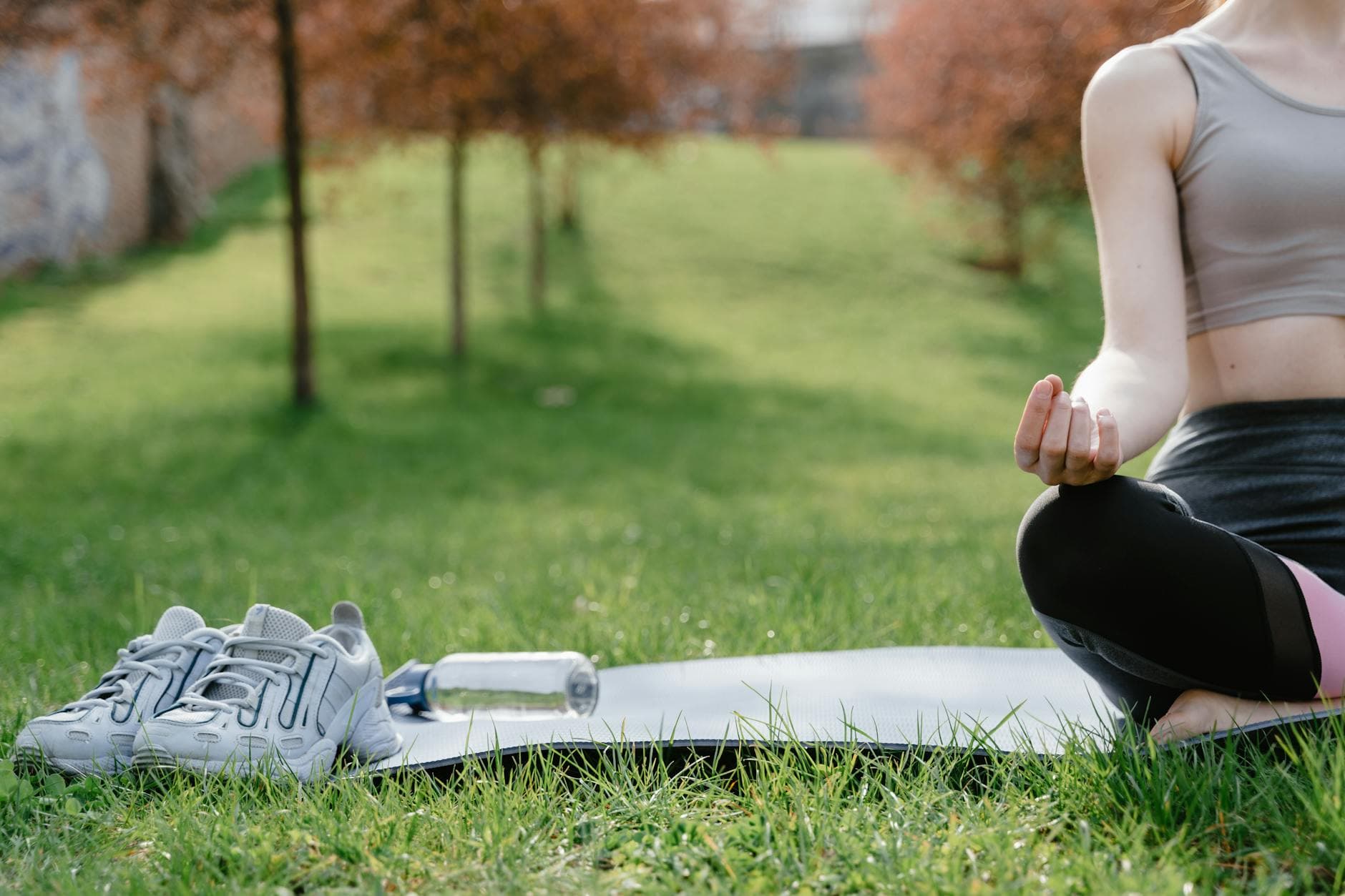 A woman in sportswear meditating on a yoga mat outdoors with shoes and water bottle nearby. - outdoor yoga spring
