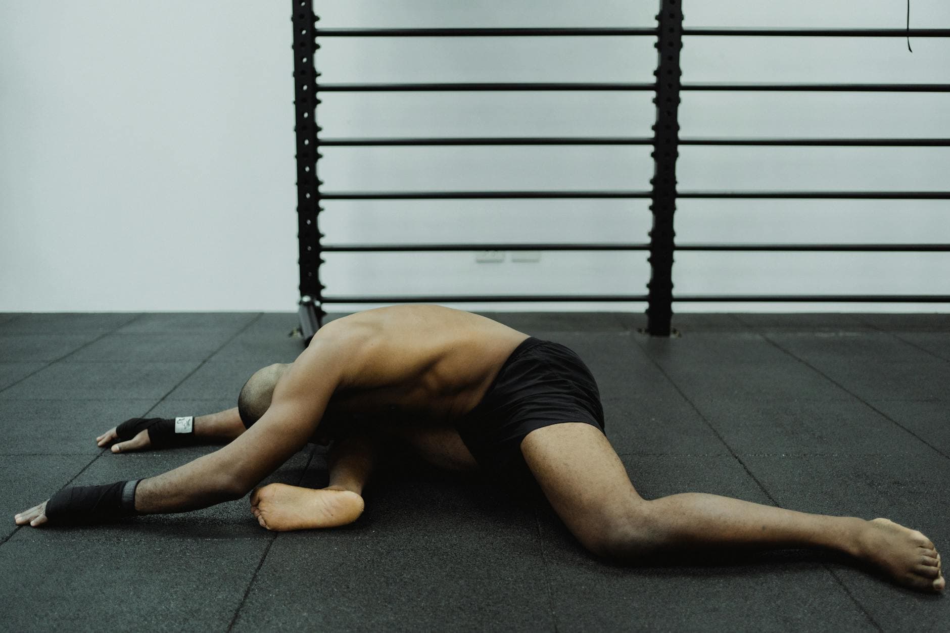 Shirtless man stretches while sitting on gym floor, showcasing flexibility. - static stretching benefits