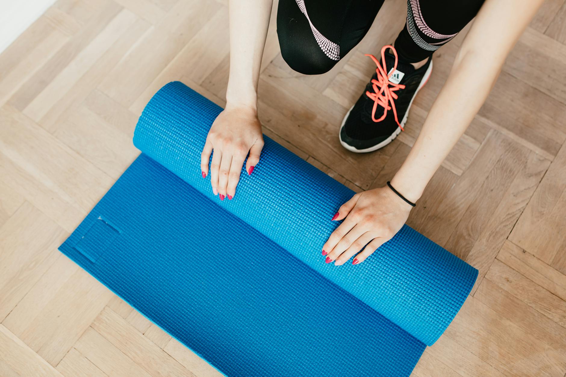 Overhead view of a woman preparing her blue yoga mat on a wooden floor, ready for exercise. - 4 day workout routine