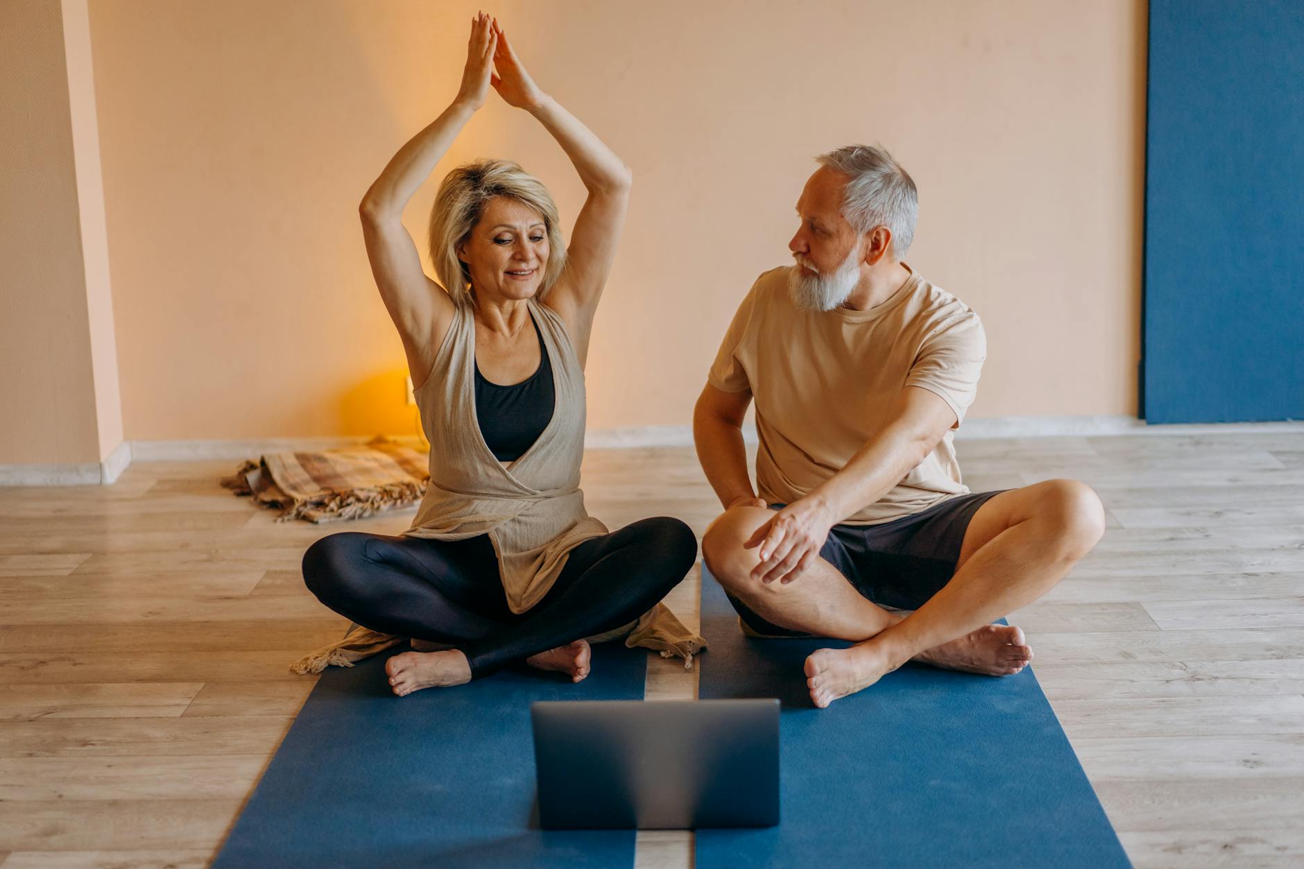 Senior couple practicing yoga together on mats indoors, using a laptop for guidance. - beginner yoga classes online