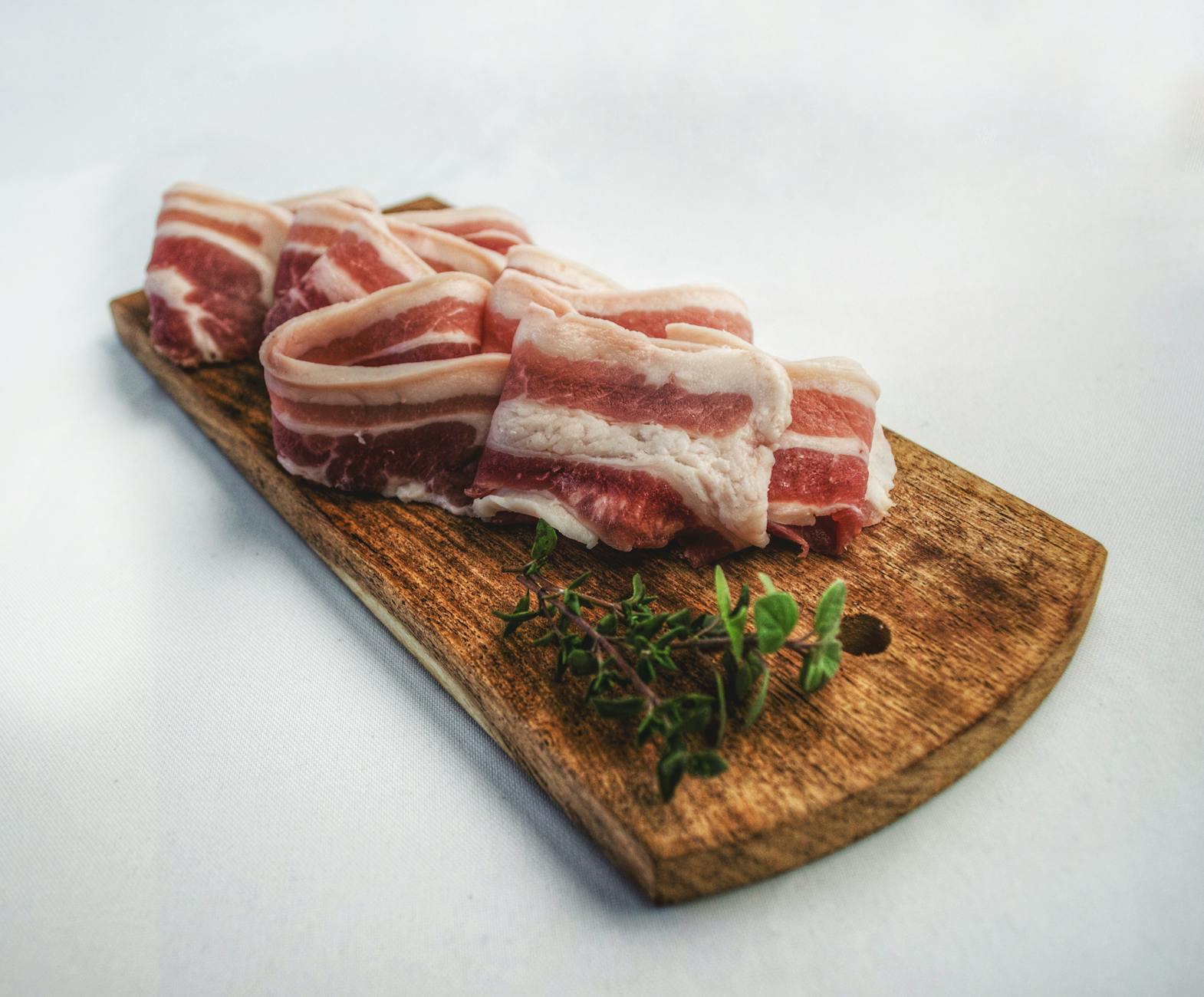Sliced bacon laid on a rustic wooden board with herbs, showcasing a delicious and inviting food presentation. - best cardio for belly fat
