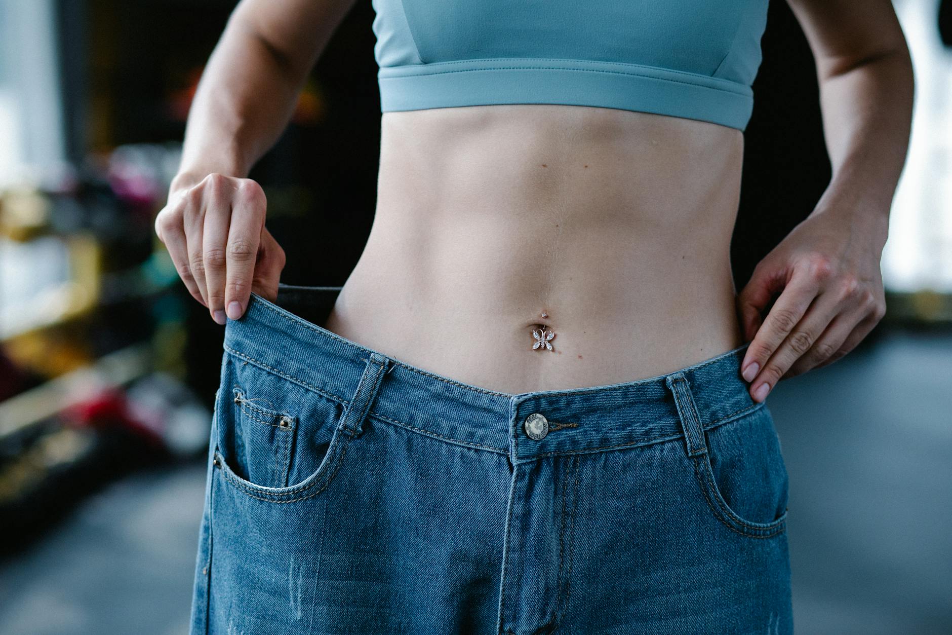 A woman shows her weight loss by holding oversized jeans revealing her toned stomach. - best cardio for belly fat