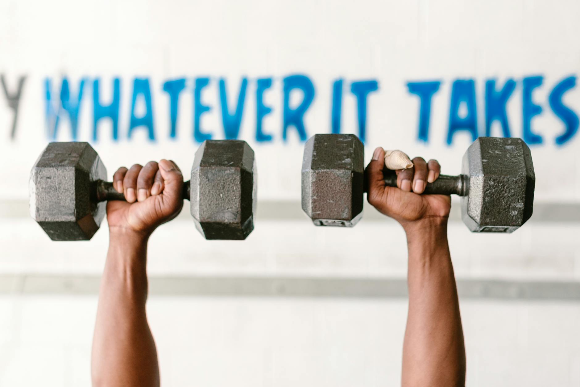 Hands holding dumbbells against motivational text "Whatever It Takes" in a gym setting. - best cardio exercises