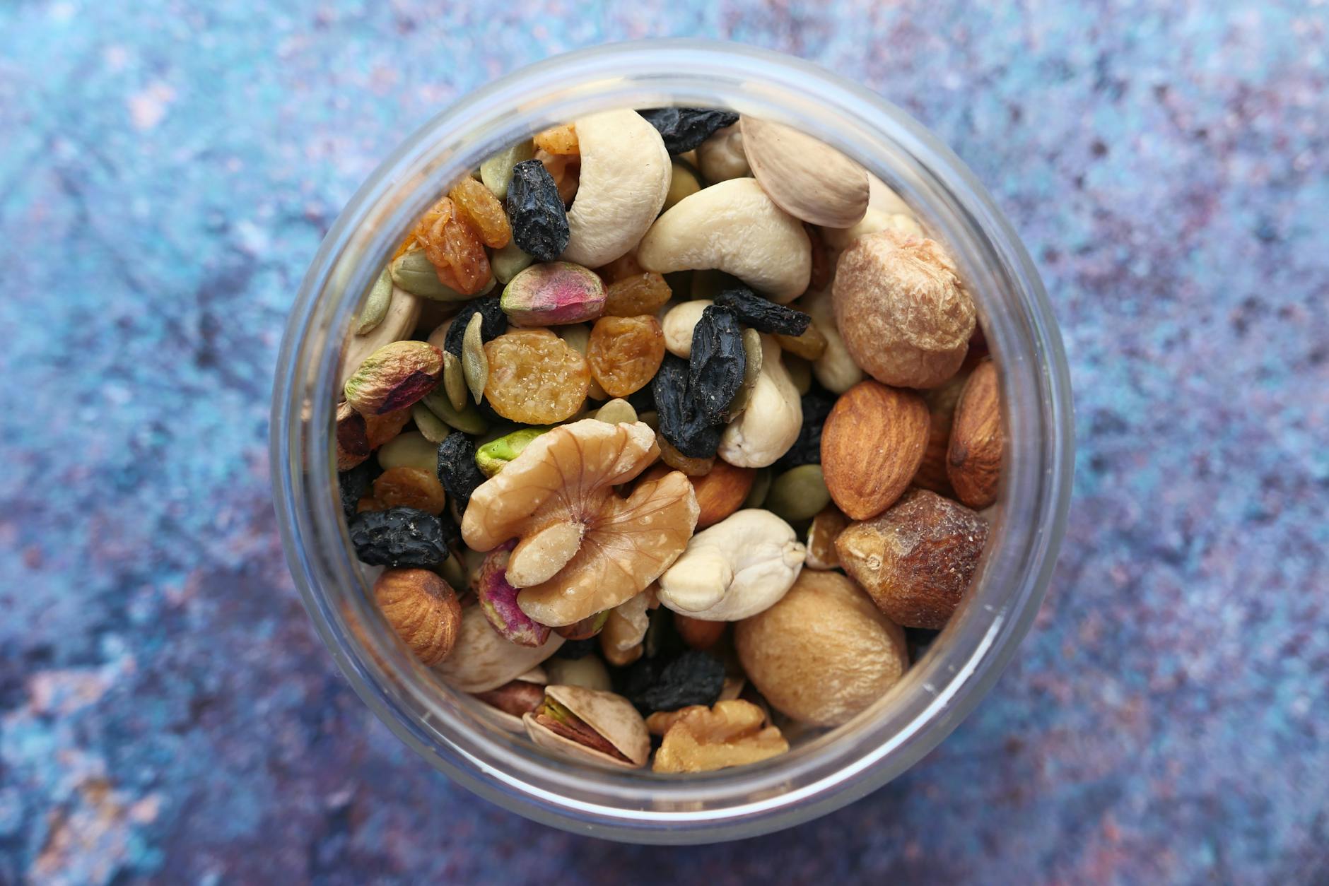 Top view of a variety of nuts and dried fruits in a jar against a blue background. - best costco healthy snacks