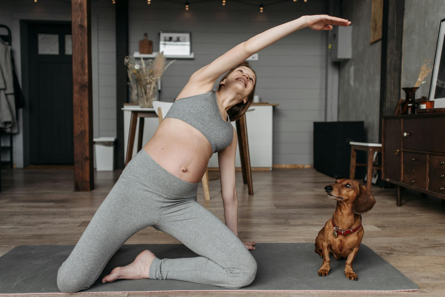 Pregnant woman practicing yoga with a dachshund indoors promoting healthy lifestyle. - best flexibility exercises