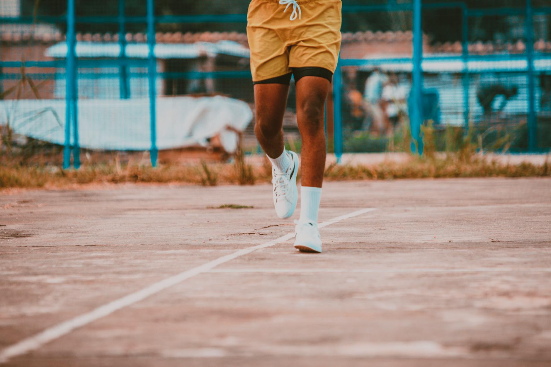 Close-up of a man's legs running on an outdoor basketball court, wearing yellow shorts and sneakers. - best at home cardio