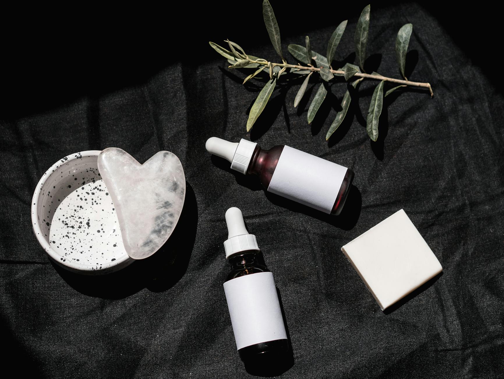 Flat lay of skincare products with gua sha and leaves on black textile. Ideal for beauty and wellness visuals. - best natural skincare products