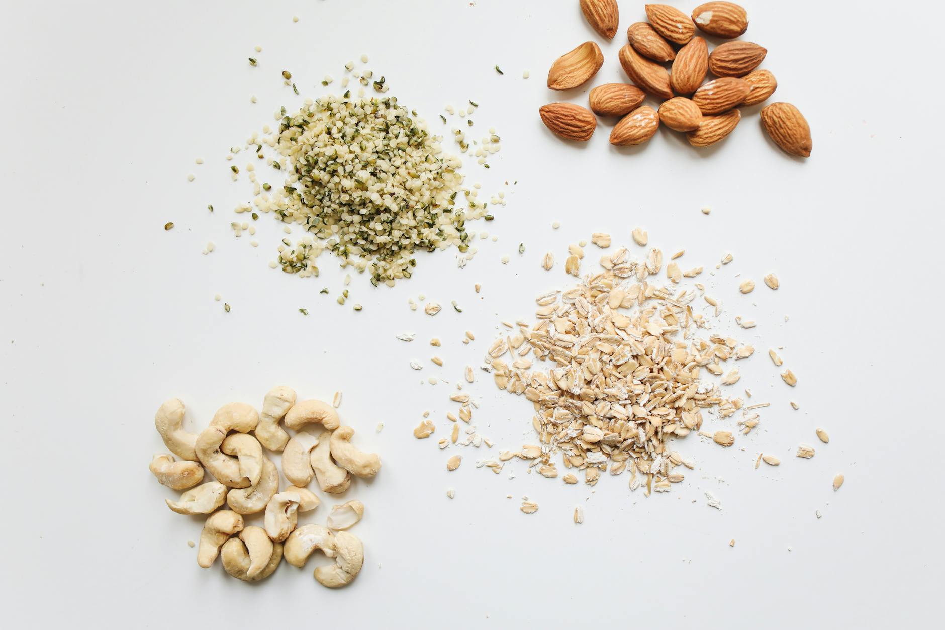 Top view of almonds, cashews, oats, and hemp seeds on white background. - best plant based protein powder