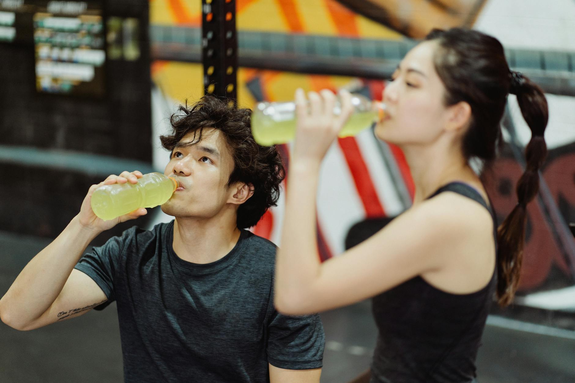 Fit Asian couple hydrating at the gym after an intense workout. Refreshing drink break. - best post workout drink