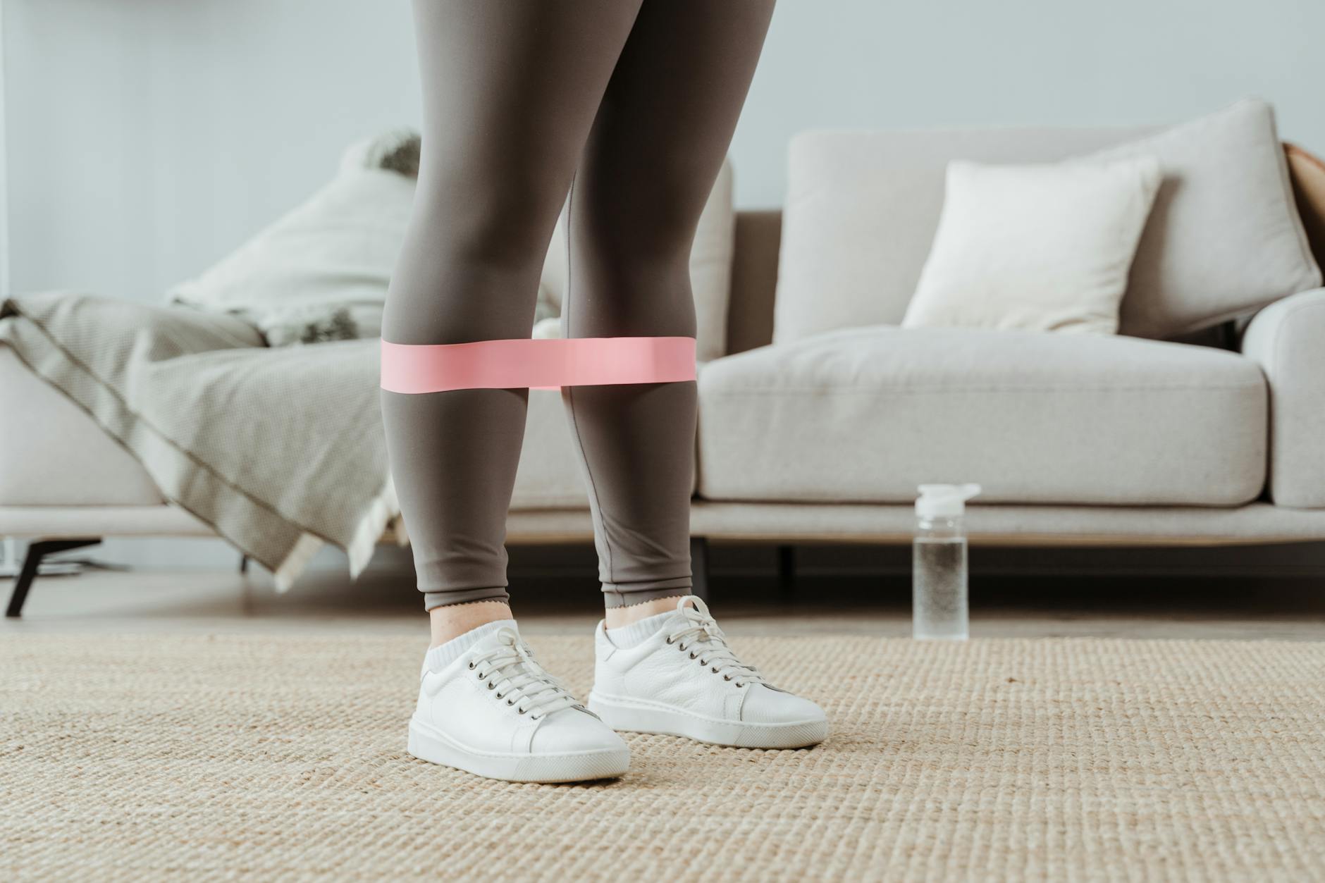 Close-up of a woman in sport leggings using a pink resistance band for leg exercises indoors. - best resistance band workout