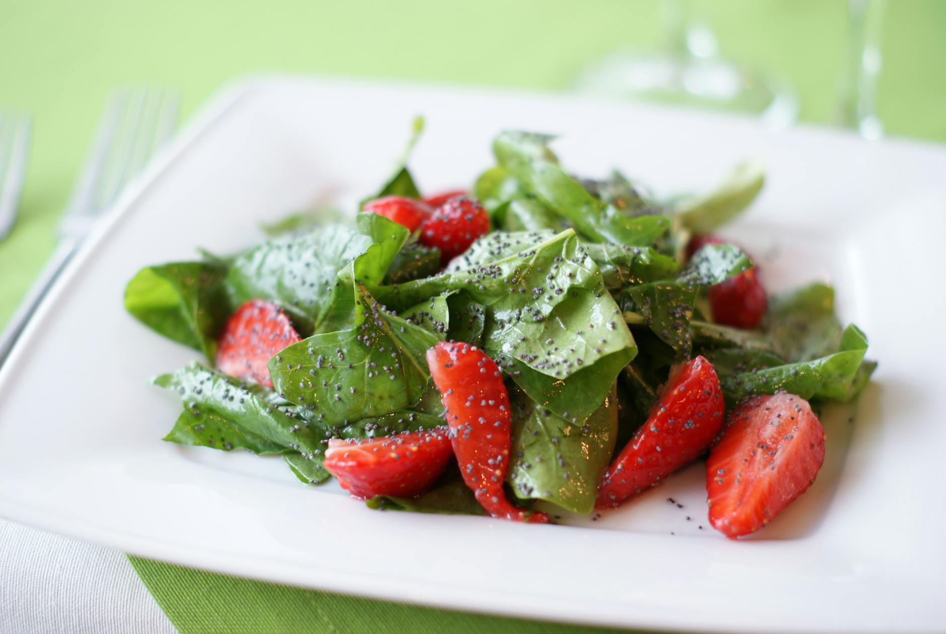 Colorful salad of fresh spinach and strawberries with poppy seeds on a plate. - bloom greens benefits