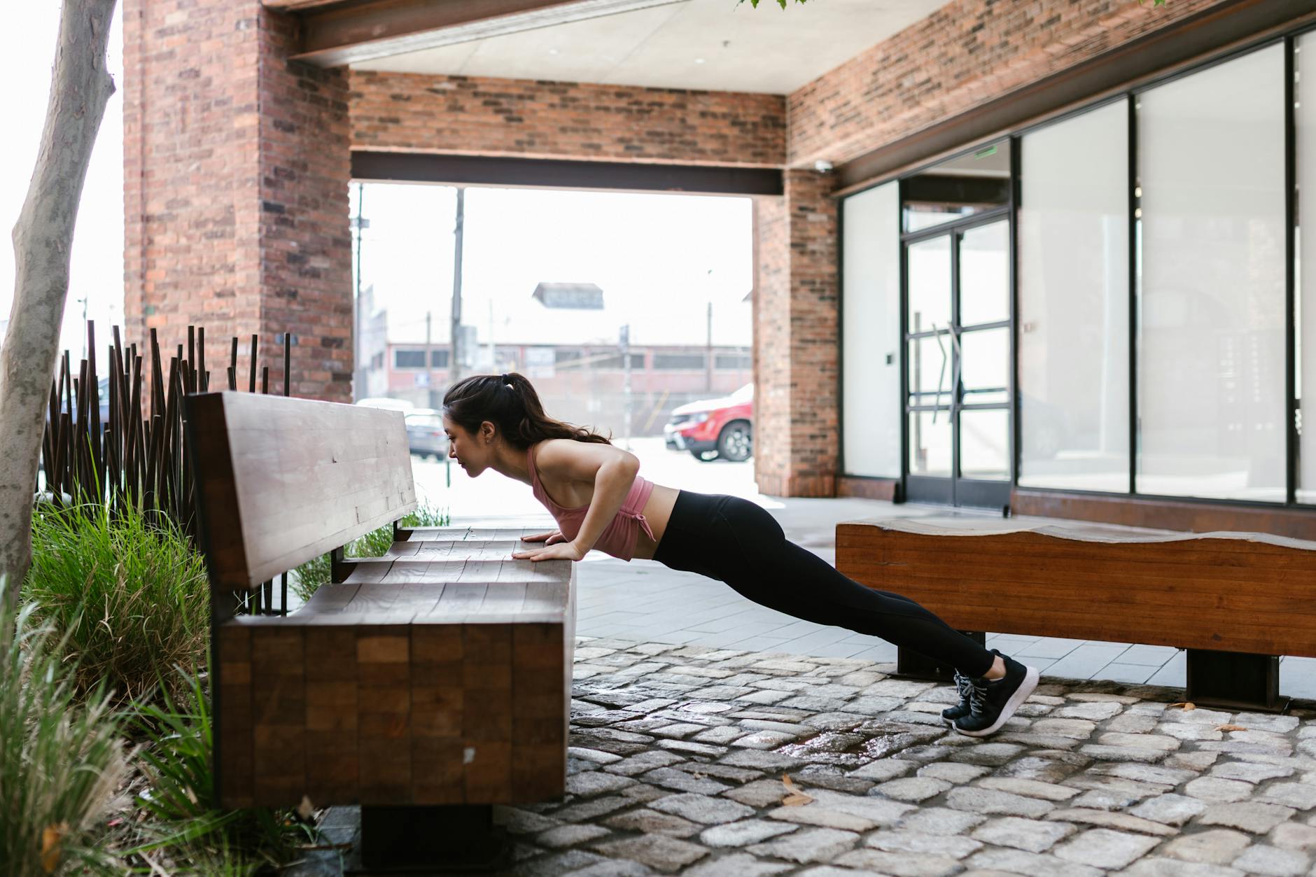 A woman doing a push-up on a bench in an outdoor urban setting, illustrating fitness and healthy living. - bodyweight muscle building