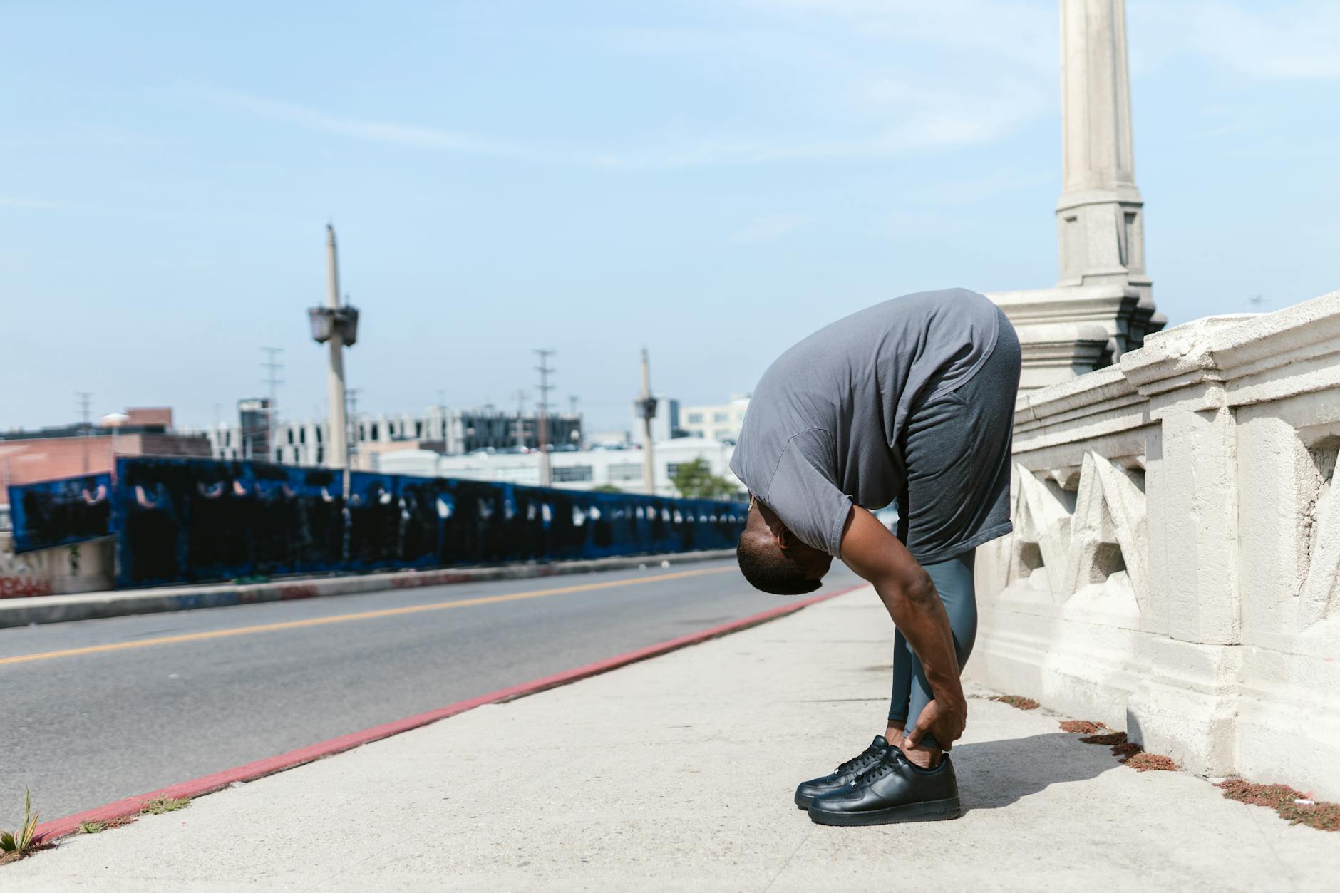 A man performing a deep stretching exercise on a city bridge, promoting fitness outdoors. - bodyweight workout routine