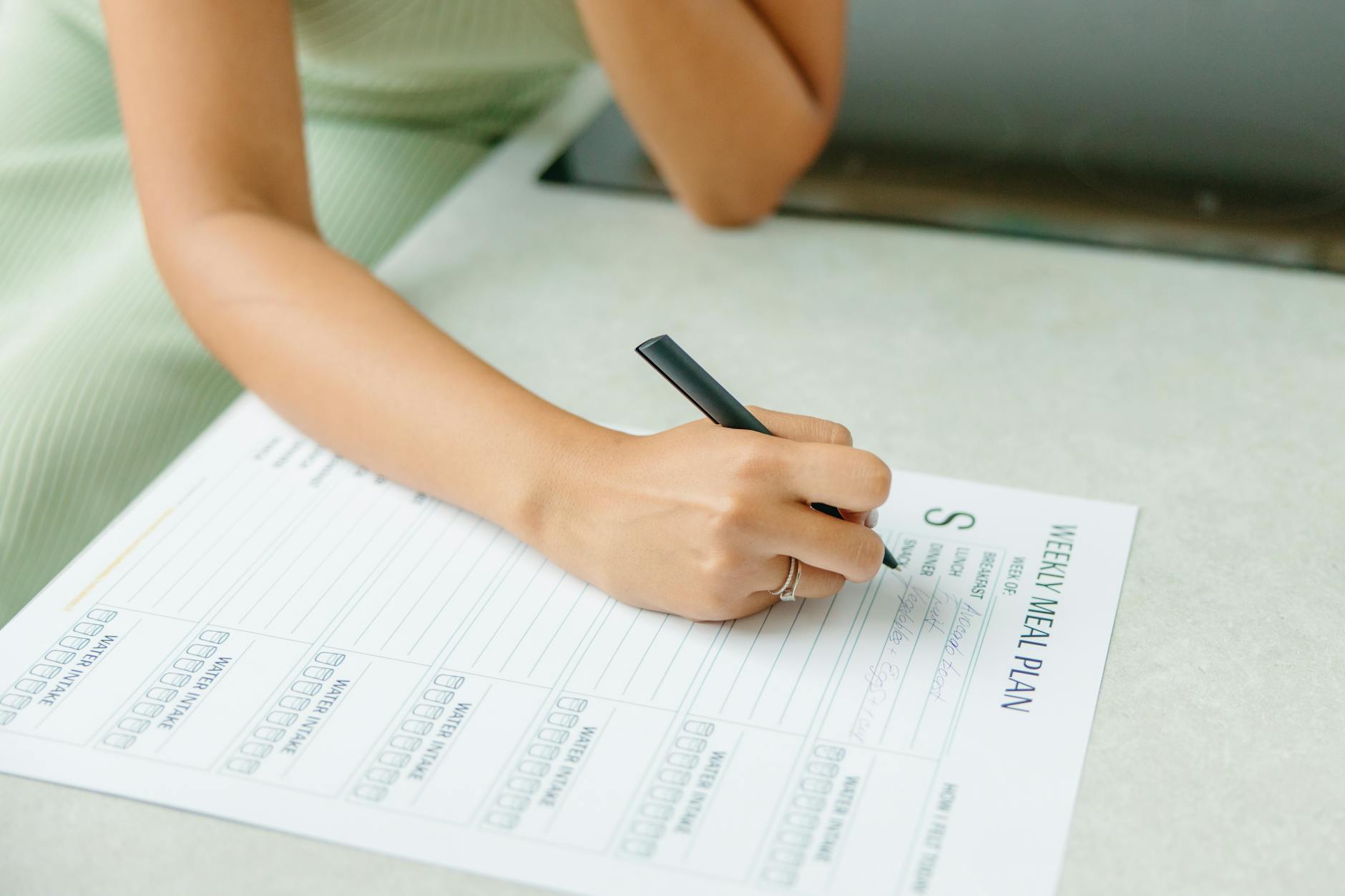 Close-up of a woman writing a weekly meal plan at home, promoting a healthy lifestyle. - budget meal plans healthy