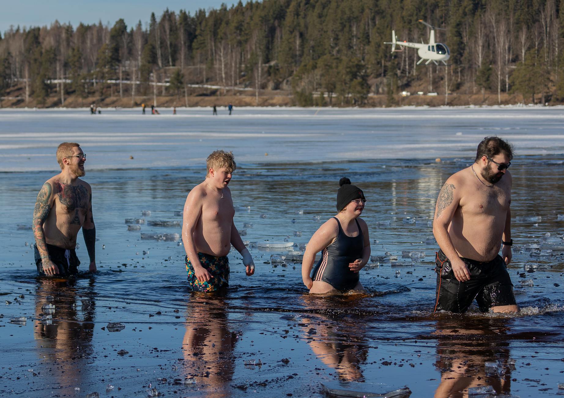 Four friends bravely plunge into a frozen lake, embracing the chilly adventure amid a winter landscape. - cold water swimming benefits