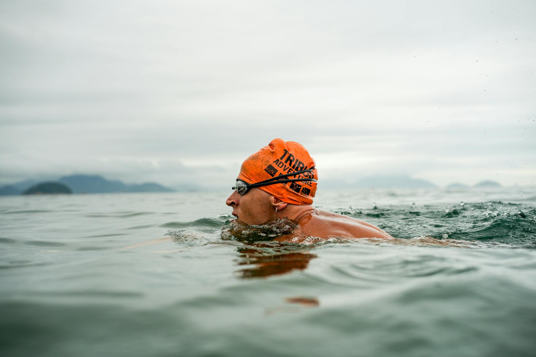 Adult male swimmer in open water wearing an orange swim cap and goggles, swimming in the sea. - cold water swimming benefits