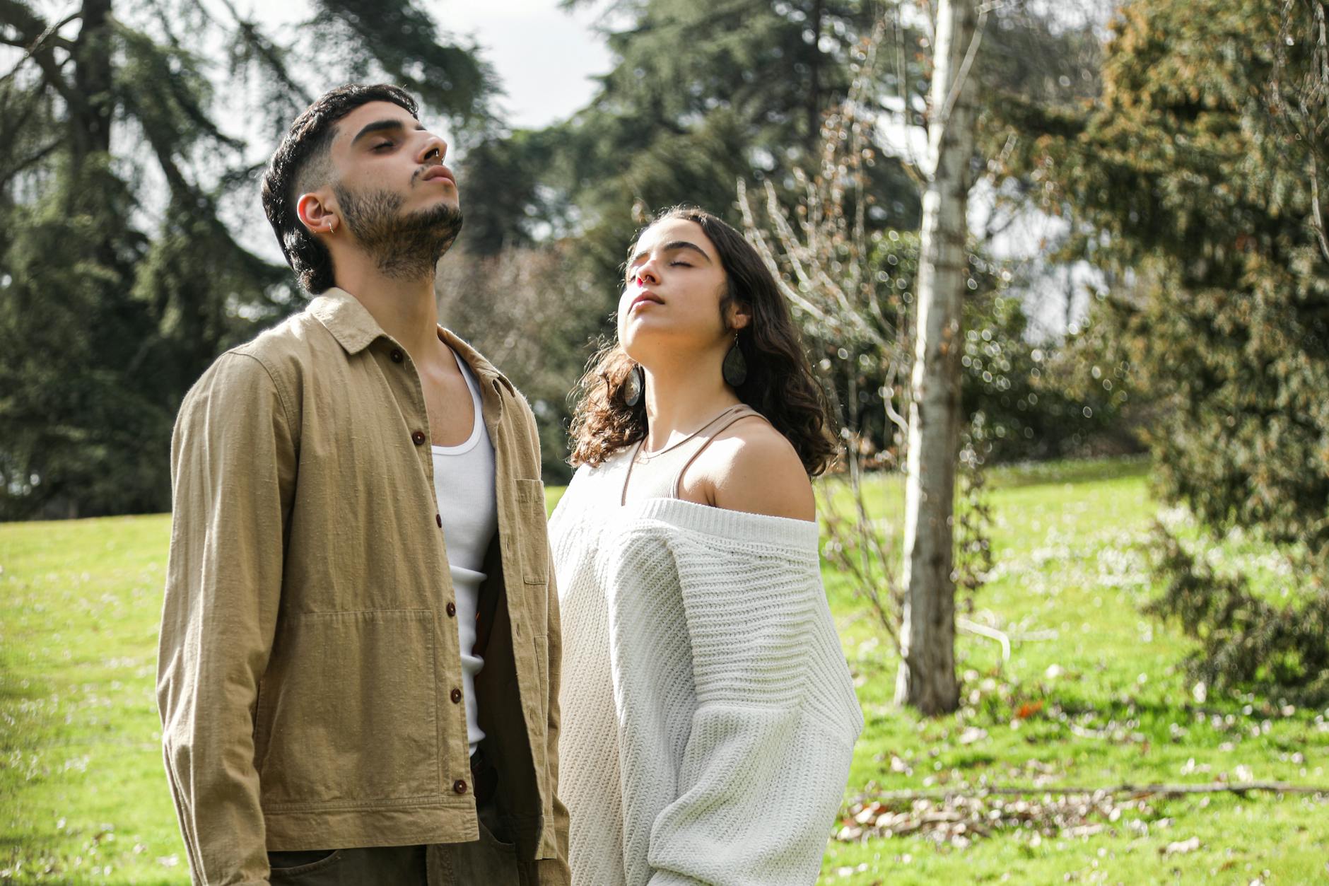 A man and woman enjoy deep breathing exercises outdoors in a lush green park.