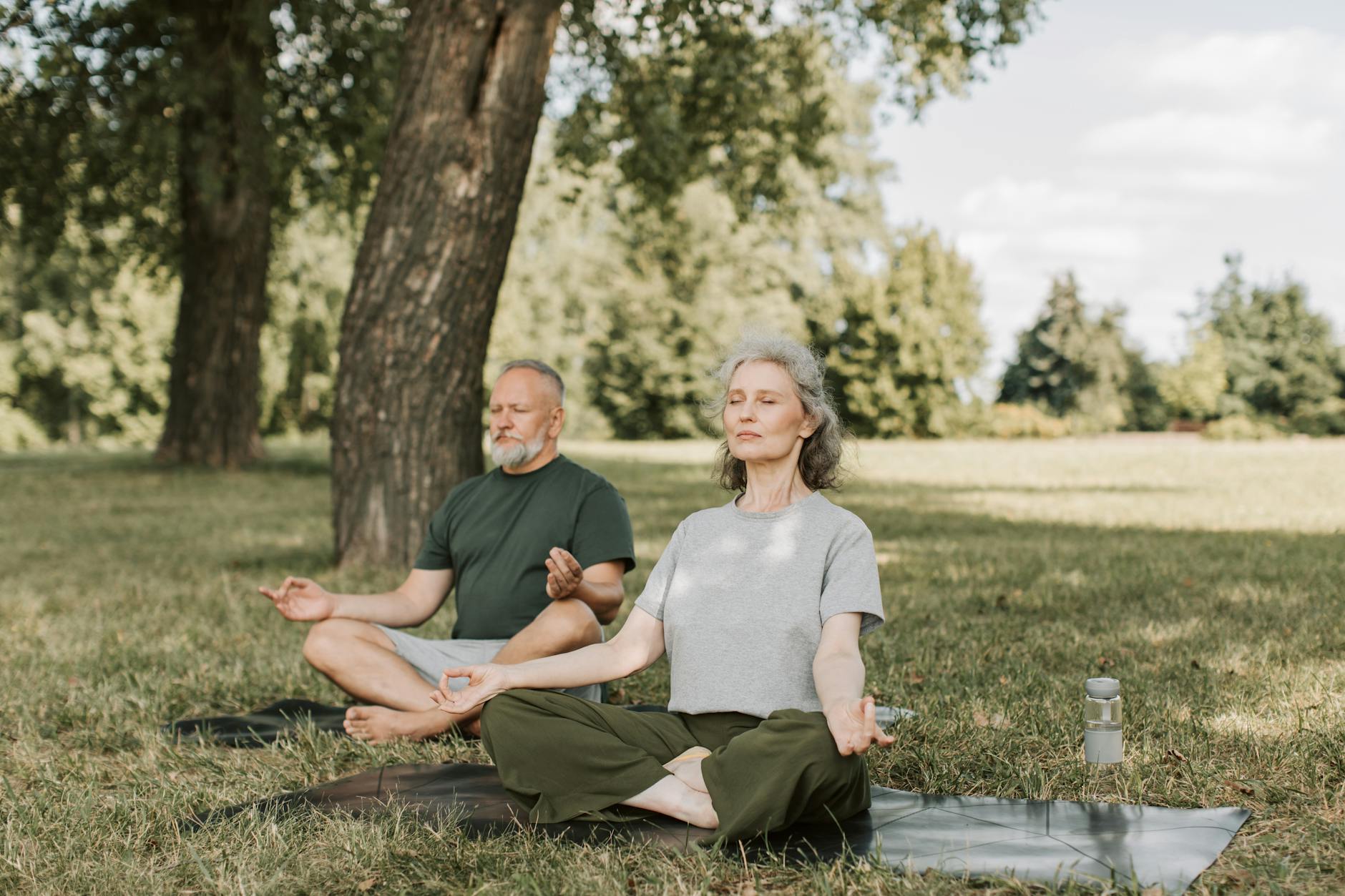Senior couple meditating on yoga mats outdoors, embracing a healthy lifestyle. - deep breathing exercises