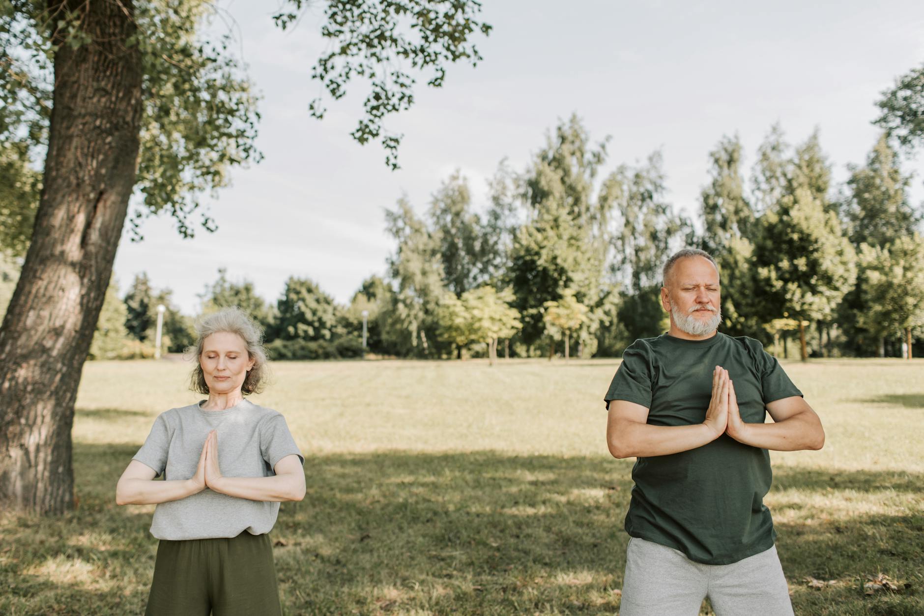 Elderly couple meditating in a calm park setting, embracing fitness and tranquility outdoors. - deep breathing exercises