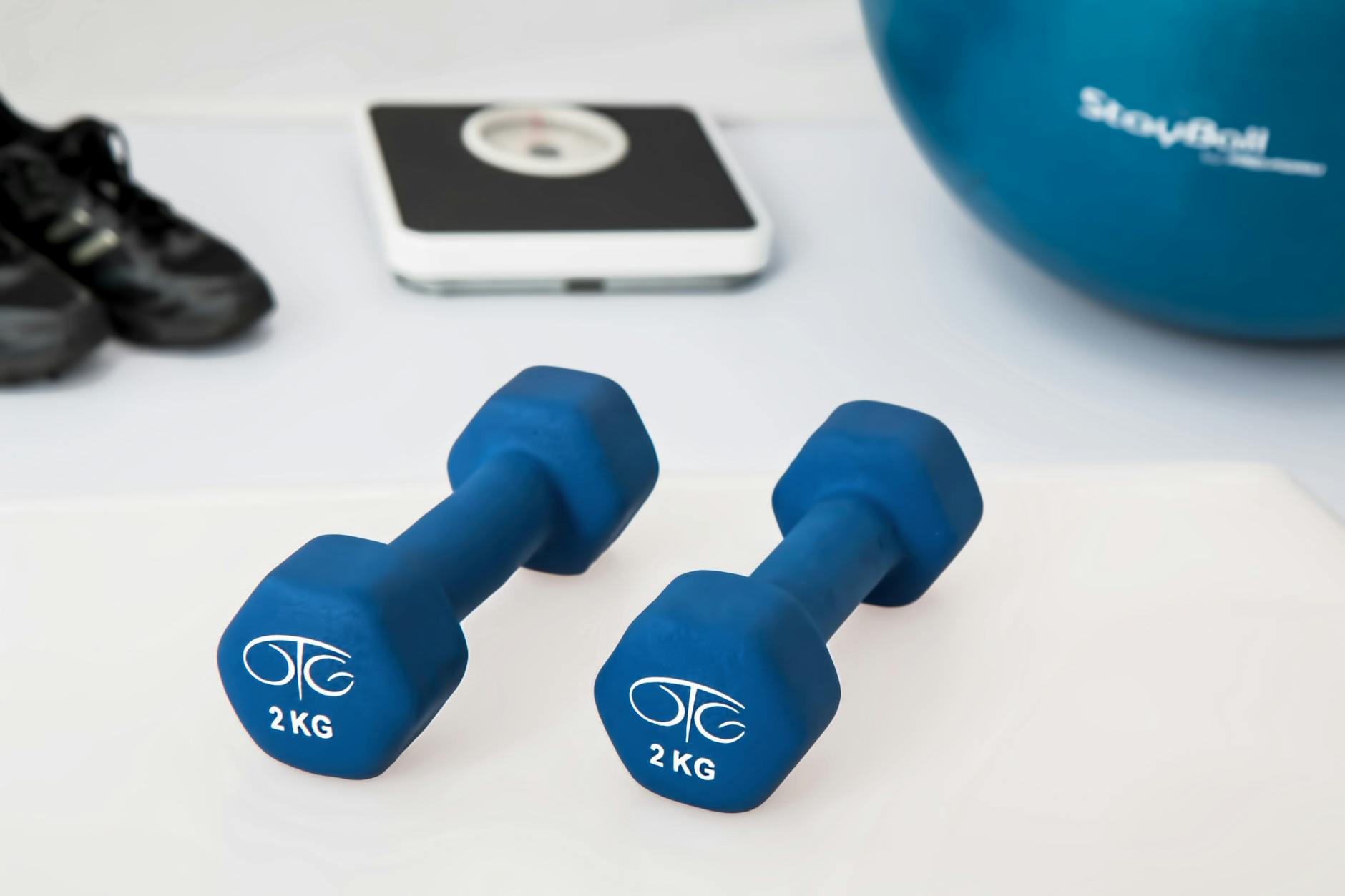 Blue dumbbells placed on a white surface with fitness equipment in the background. - dumbbell good morning
