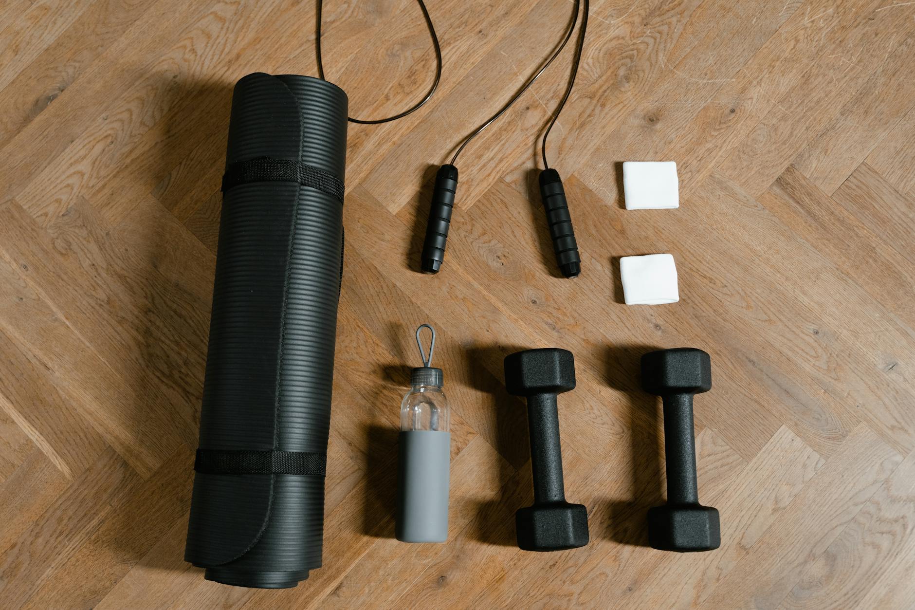 Flat lay of exercise essentials including dumbbells, yoga mat, and water bottle on wooden floor. - dumbbell good morning