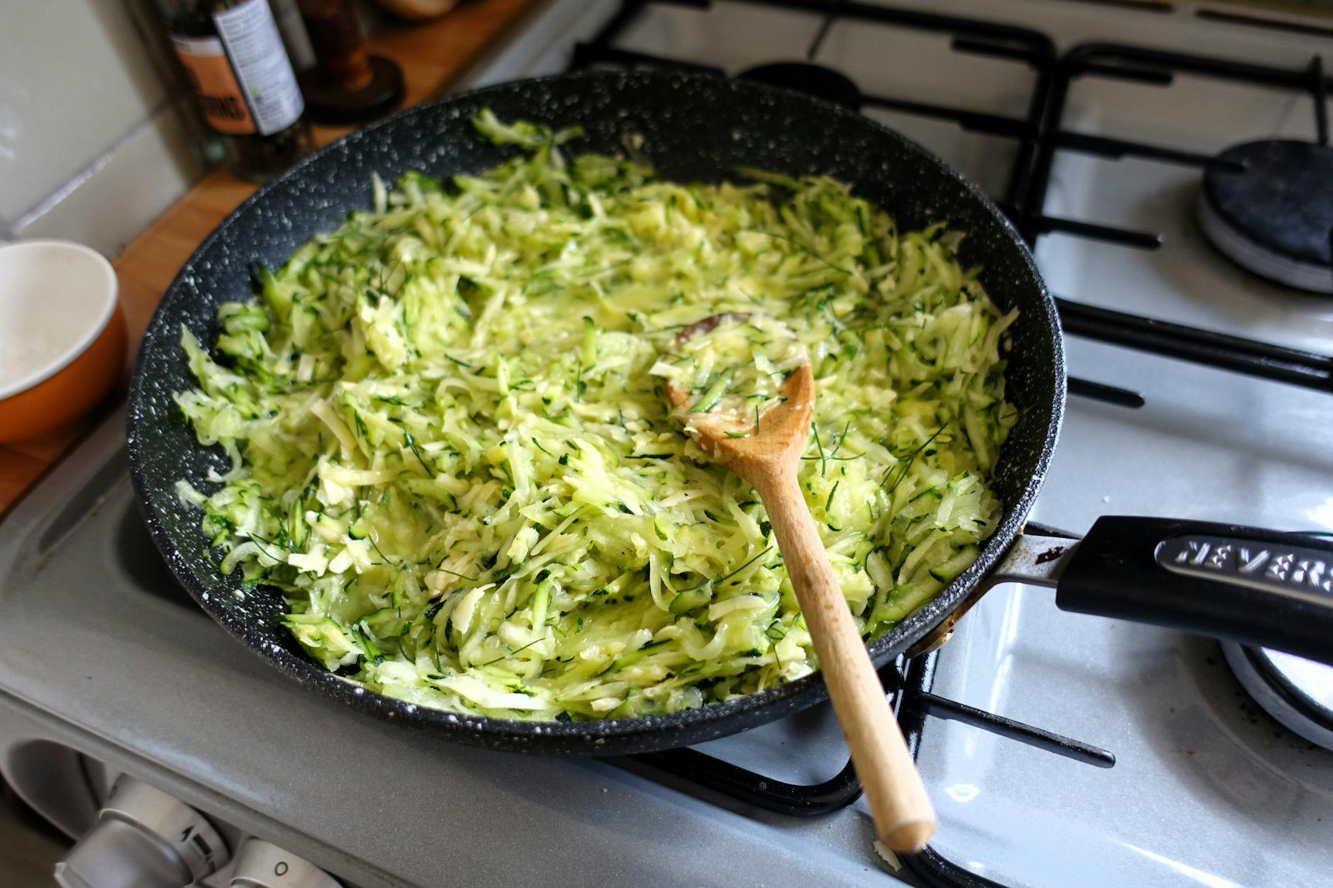 Freshly shredded zucchini cooking in a frying pan on a modern kitchen stove. - easy dinner recipes