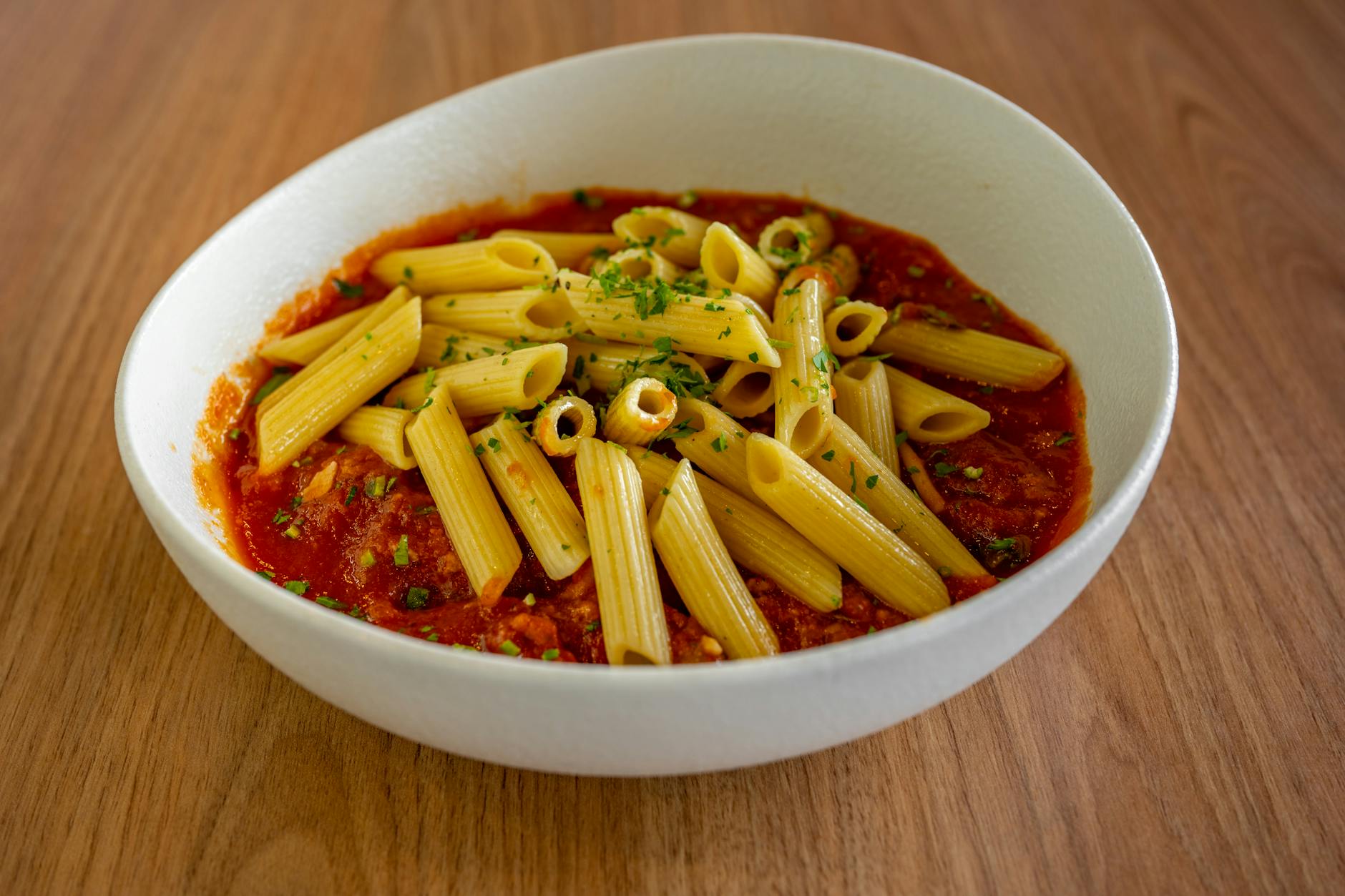 Penne pasta served in a flavorful tomato sauce, garnished with herbs, in a white bowl on a wooden table. - easy dinner recipes
