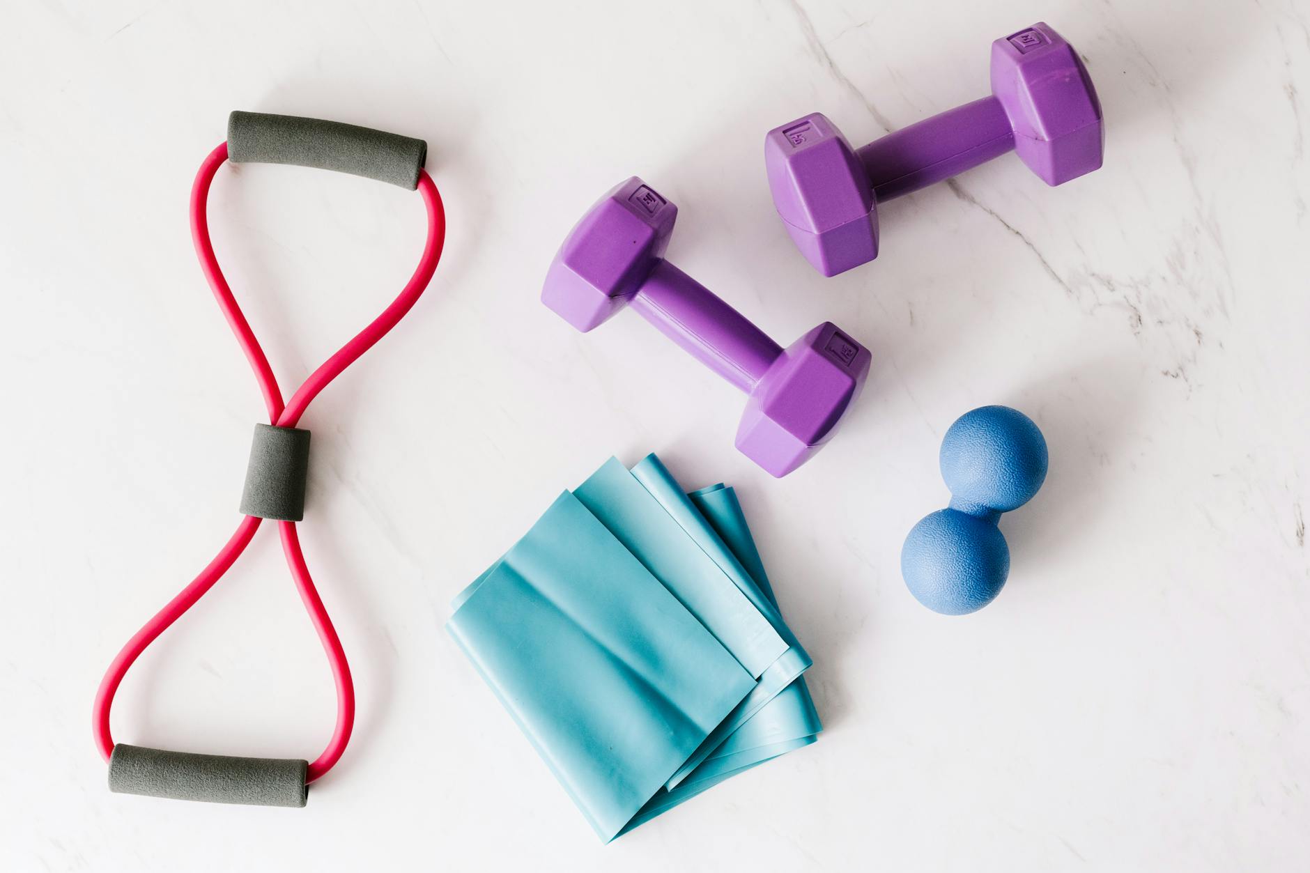 Colorful home workout equipment, including dumbbells and resistance bands, on a marble surface. - no equipment home workout