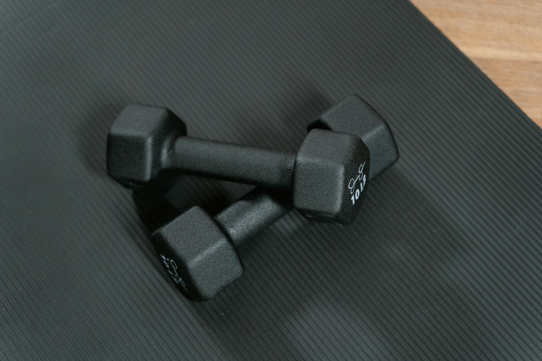 Black dumbbells placed on a yoga mat, perfect for home workouts and strength training. - no equipment home workout