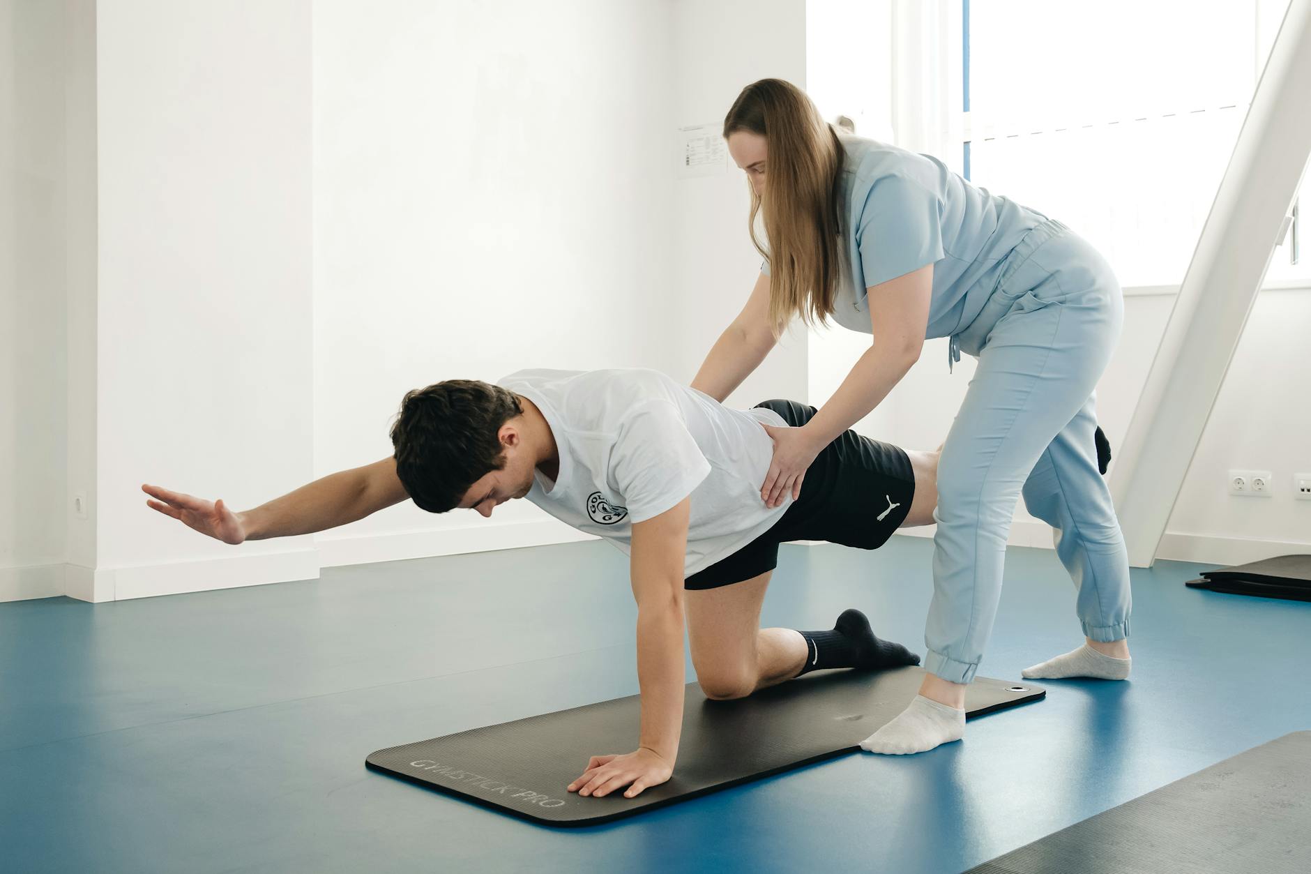 A physiotherapist guides a patient's exercise on a mat in a Vilnius gym. - exercises for posture correction