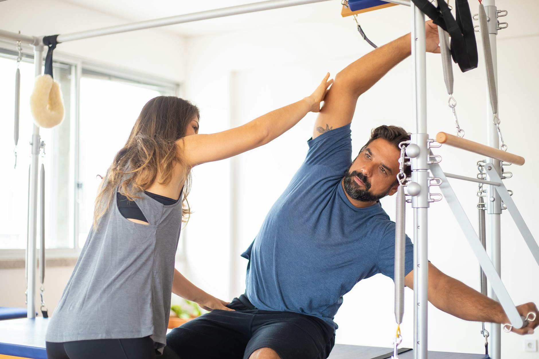 Trainer guides client on reformer machine during pilates session in a bright gym setting. - exercises for posture correction