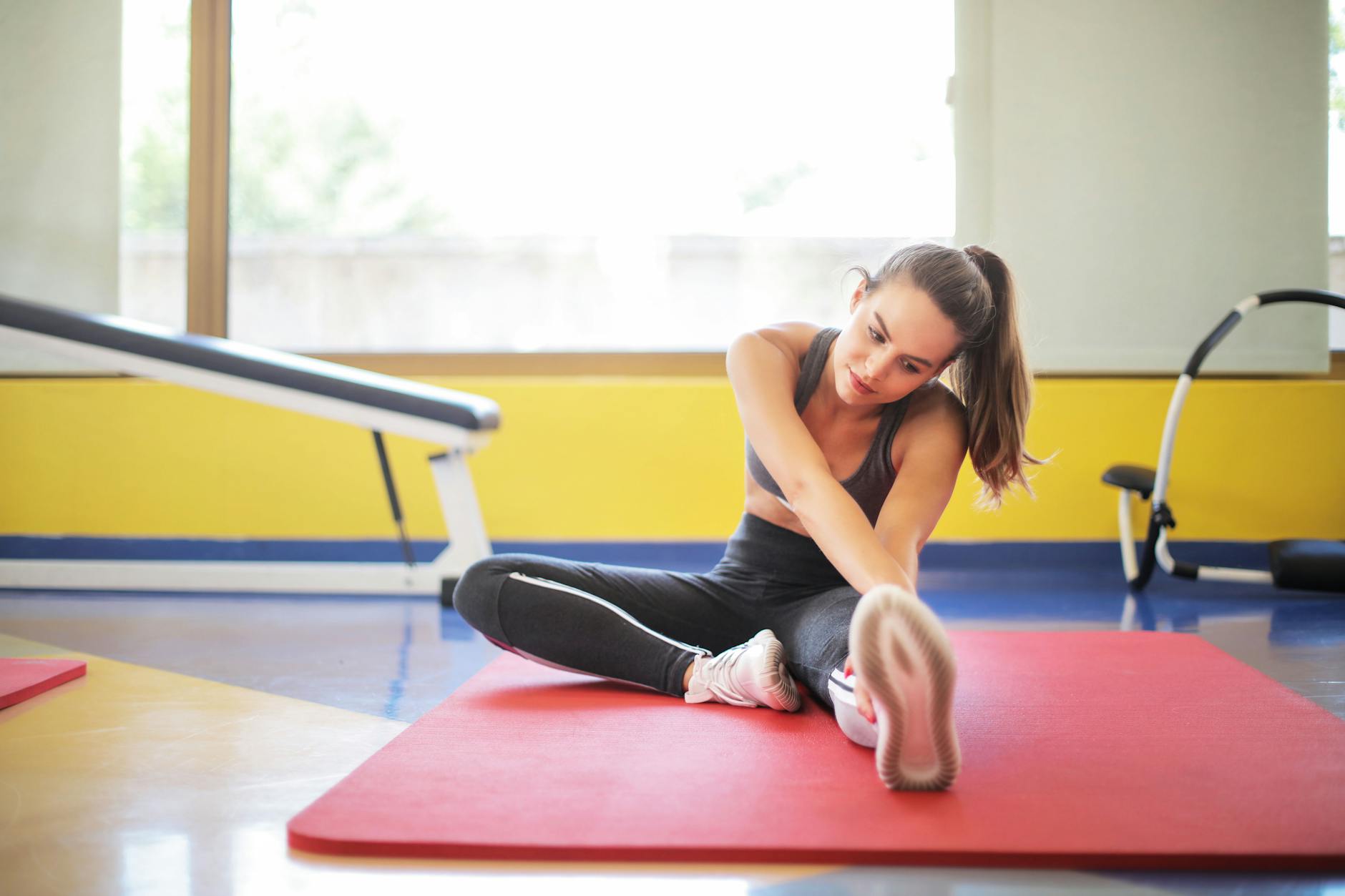 Female athlete stretching on a red yoga mat indoors, emphasizing flexibility and fitness. - flexibility exercise examples
