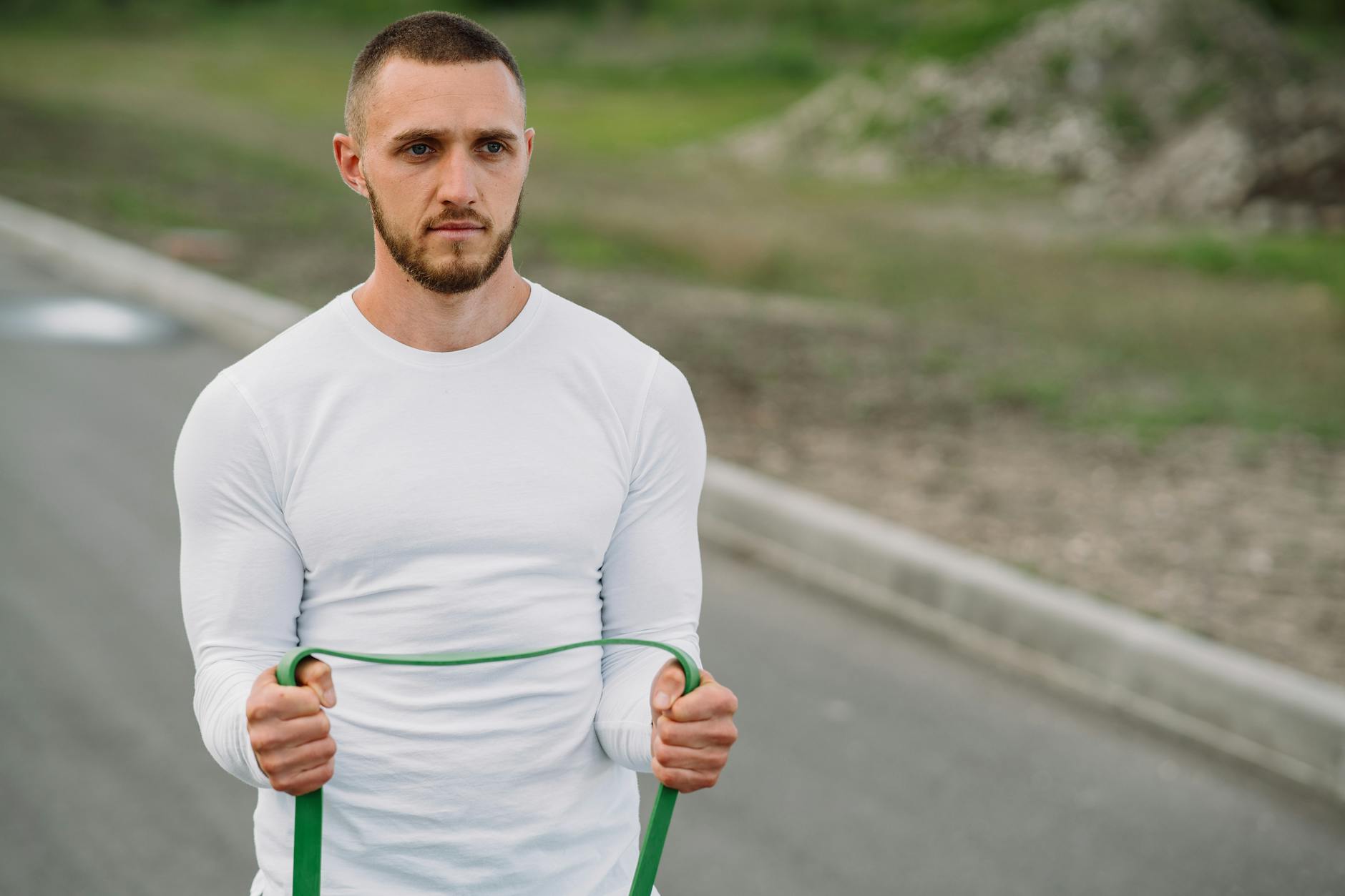 Adult man working out with a resistance band on an outdoor road. - full body resistance band workout