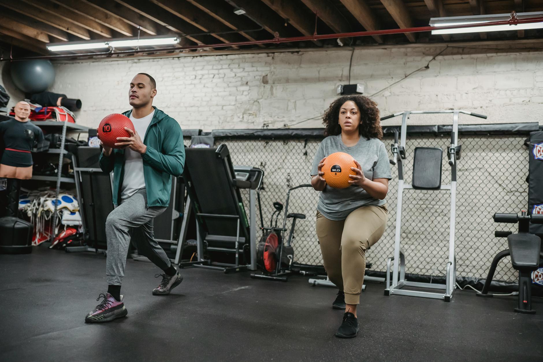 Two people doing lunges with medicine balls in a gym, showcasing focus and fitness. - full body weight workout