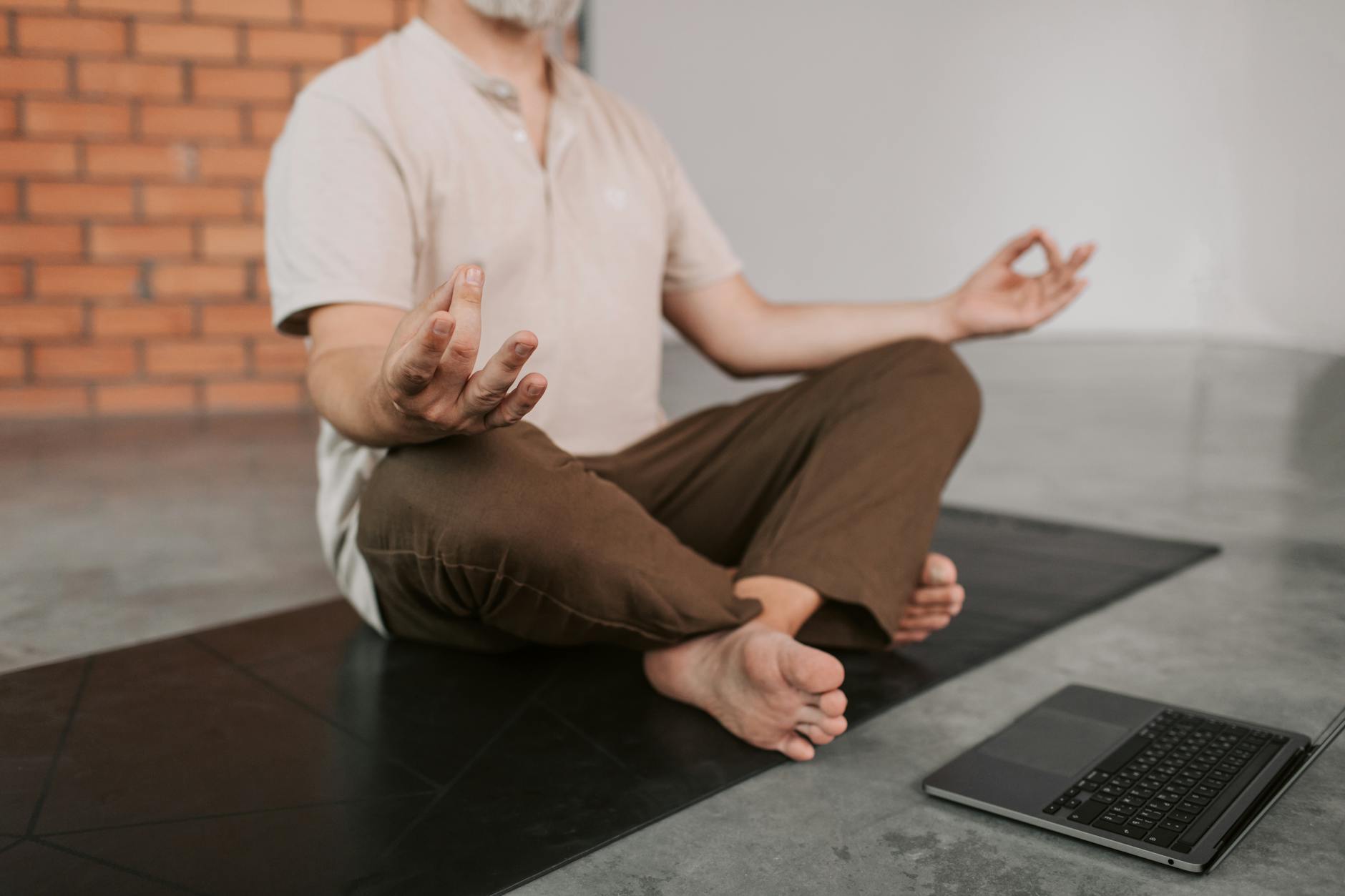 Senior man practicing yoga indoors on a mat, accompanied by a laptop for a virtual session. - guided mindfulness meditation youtube