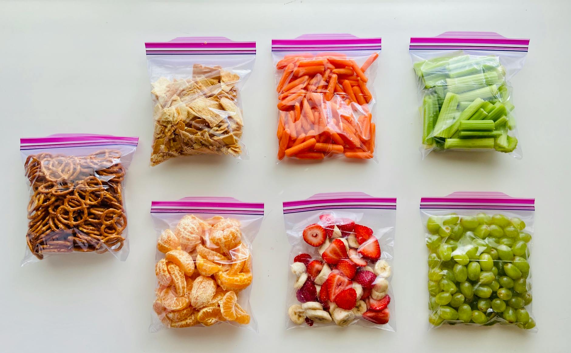 An assortment of fruits, vegetables, and snacks neatly packed in zip lock bags on a white background. - healthy meal plan ideas