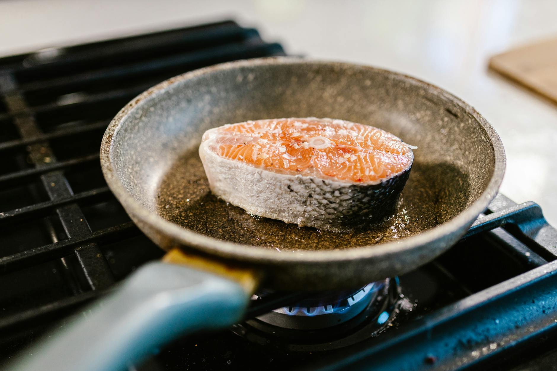 A salmon steak is searing in an iron frying pan on a stove, showcasing cooking detail. - healthy salmon recipes