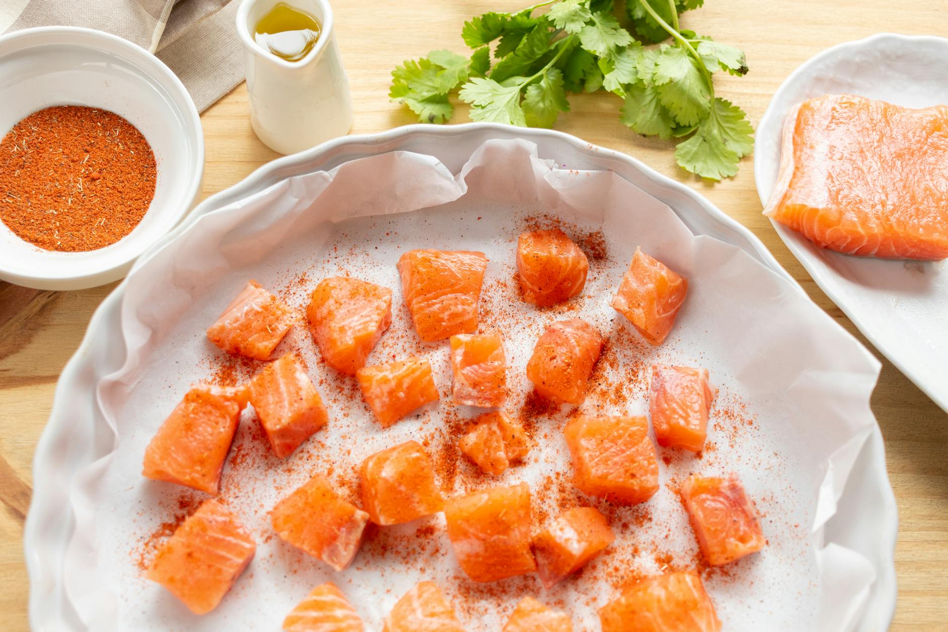 Fresh salmon cubes seasoned with spices ready for cooking, garnished with cilantro on a wooden surface. - healthy salmon recipes