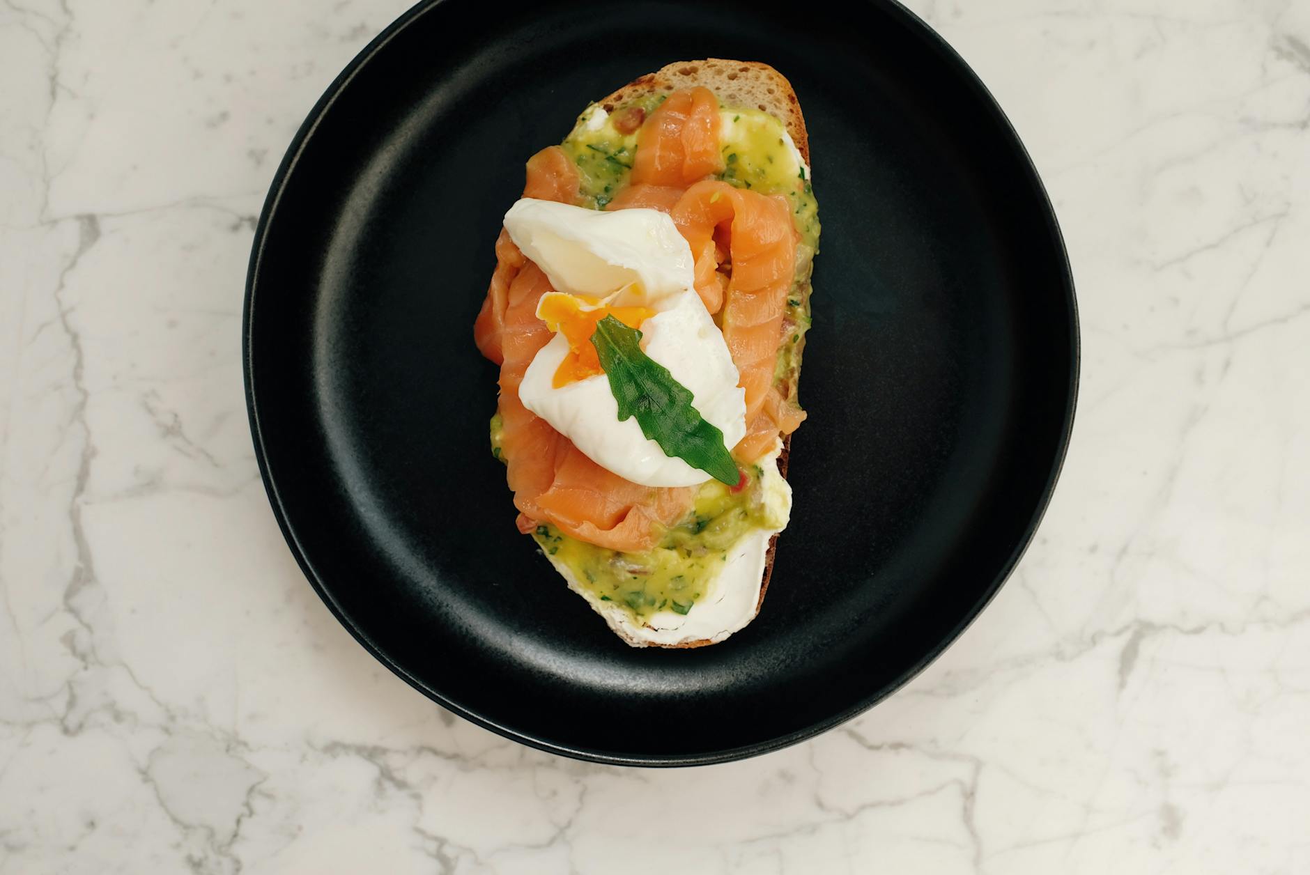 Top view of black ceramic plate with tasty toast with salmon and poached egg served on white marble table - healthy salmon recipes