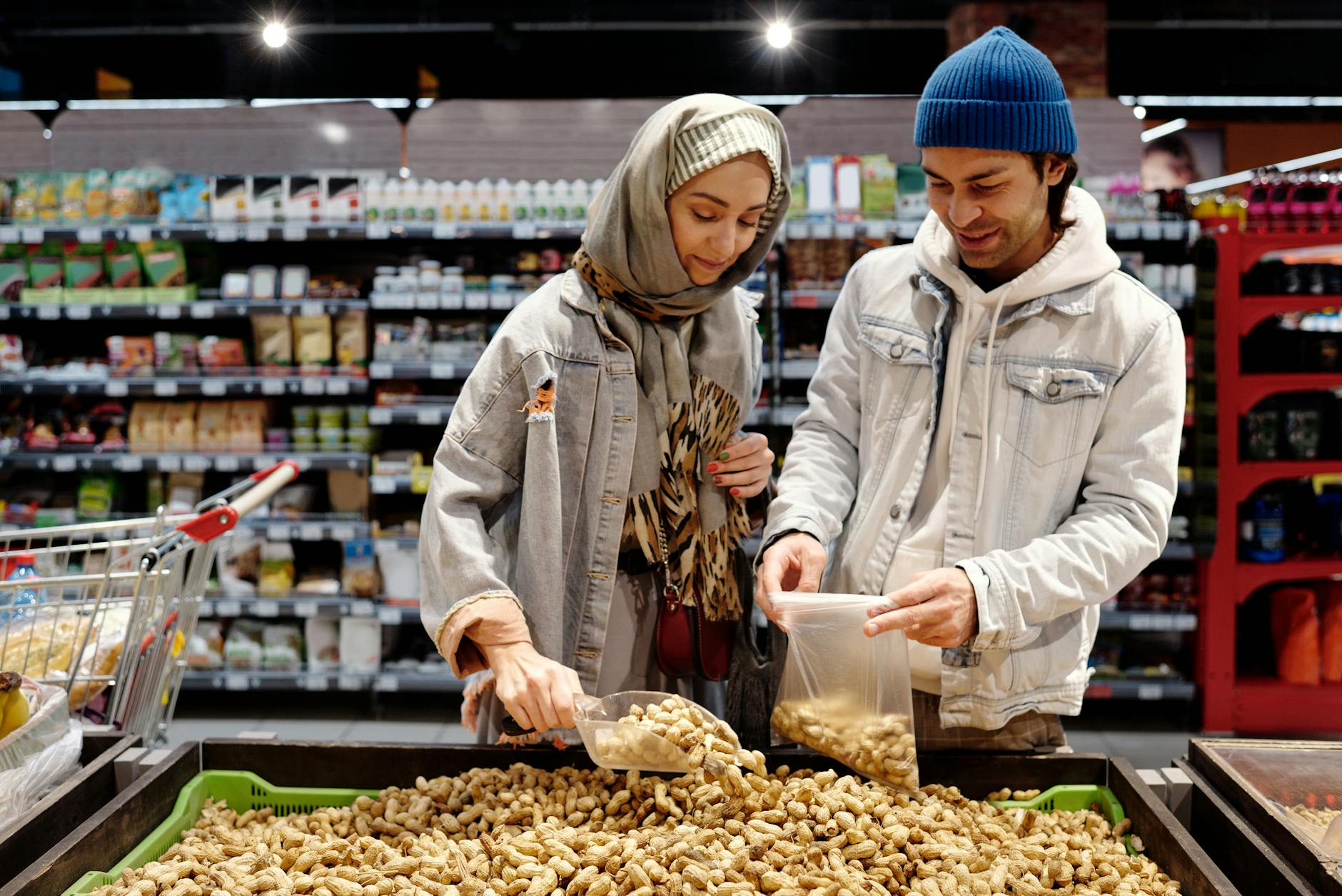 A man and woman select peanuts in a grocery store aisle during a shopping trip. - healthy snacks to buy