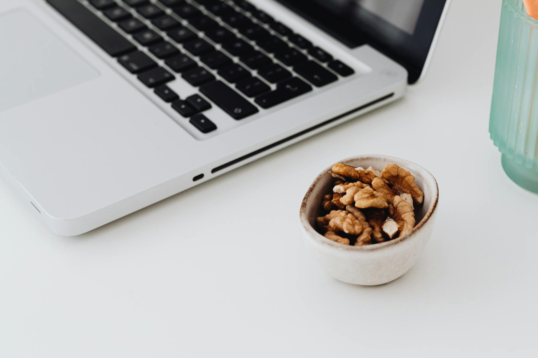 A minimalistic work desk setup featuring a laptop and a bowl of healthy walnuts for snacking. - healthy work snacks